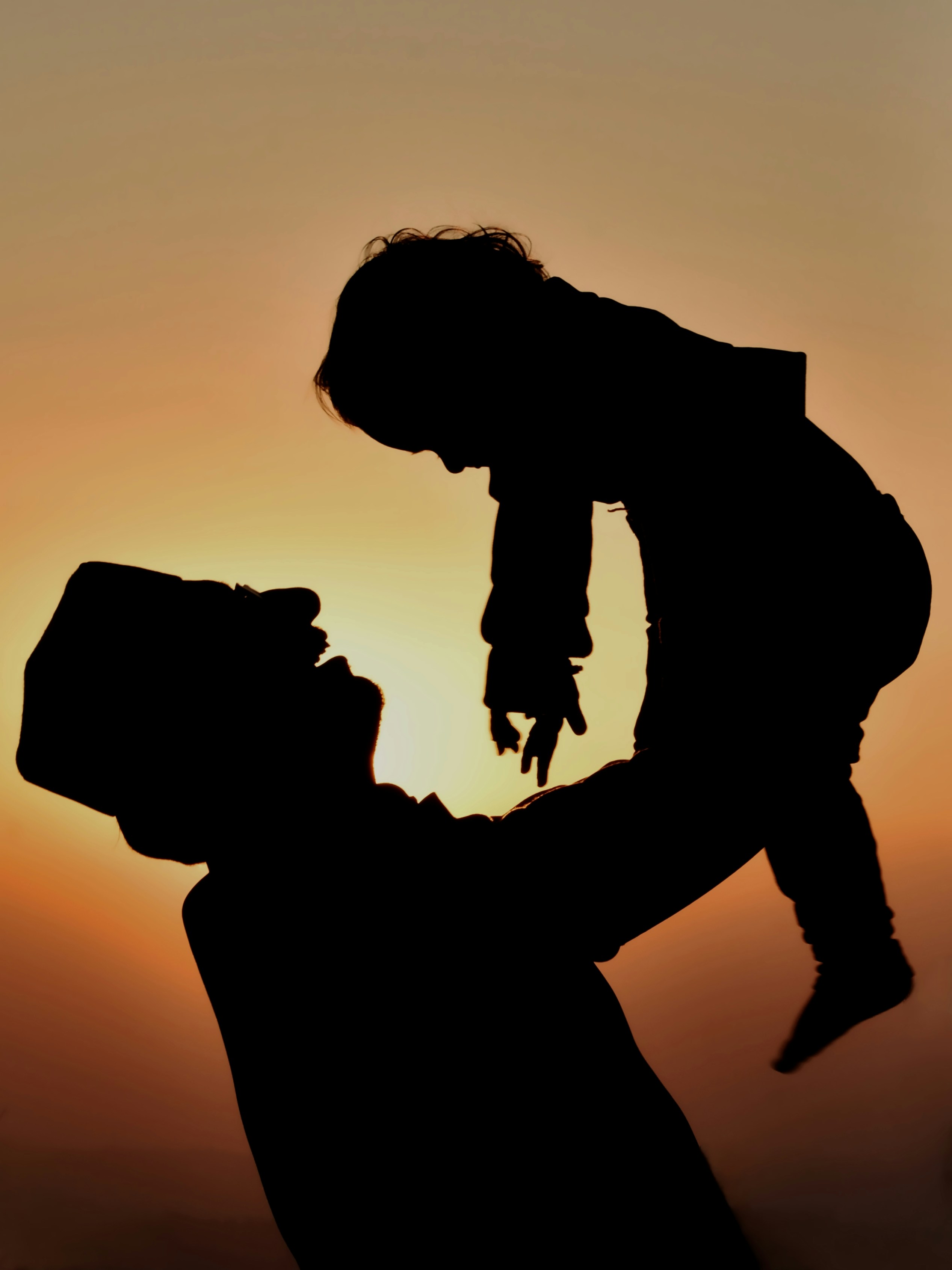 Father holding child up against sunset