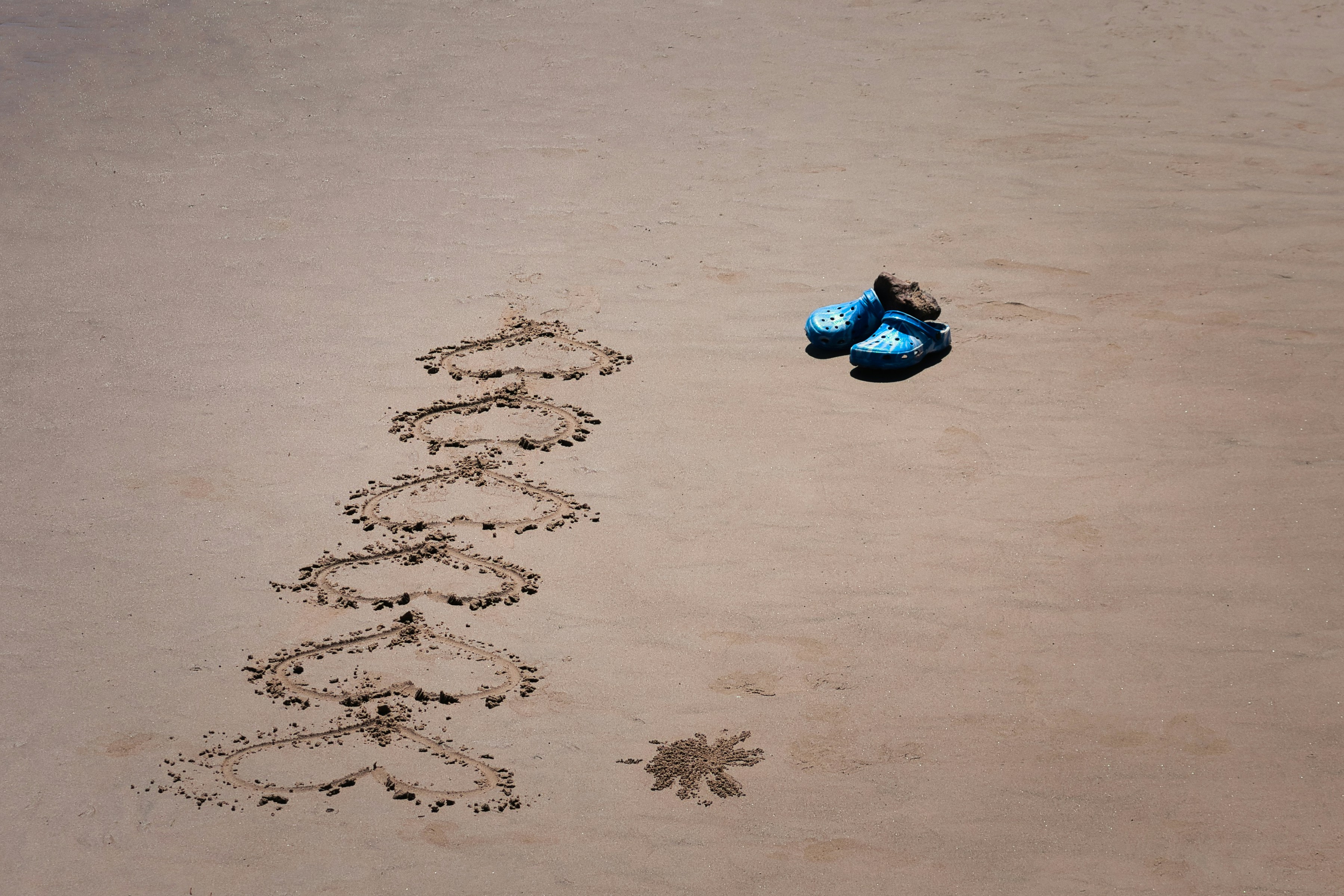 Hearts drawn in sand with a pair of blue flip-flops.