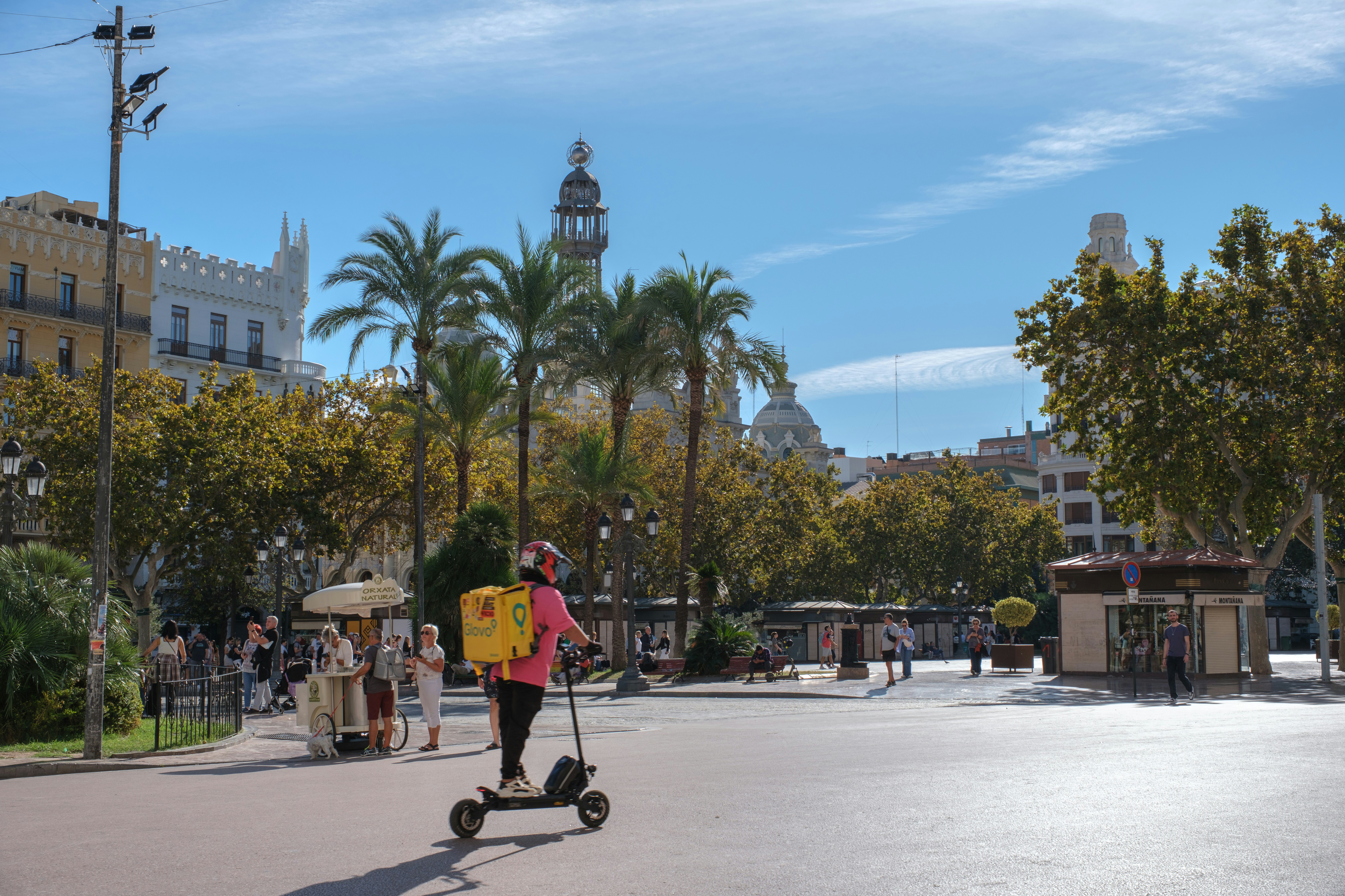 Person riding electric scooter in sunny city square.