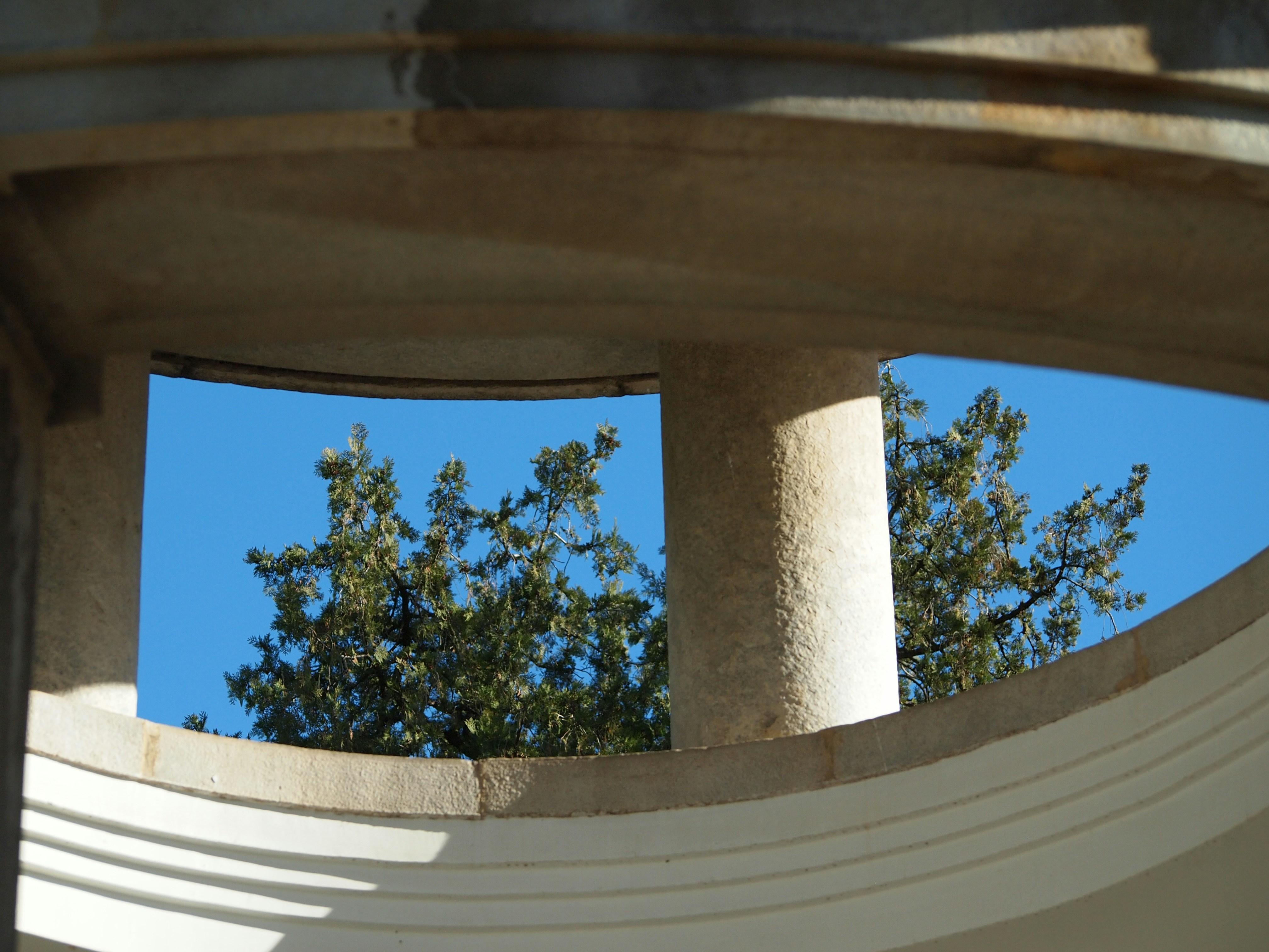 Trees and blue sky seen through architectural opening.