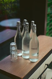 Glass bottles of water and stacked glasses on a bar.