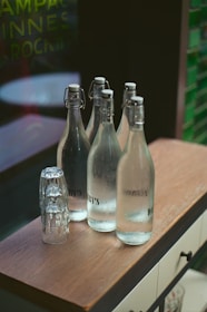Glass bottles of water and stacked glasses on a bar.