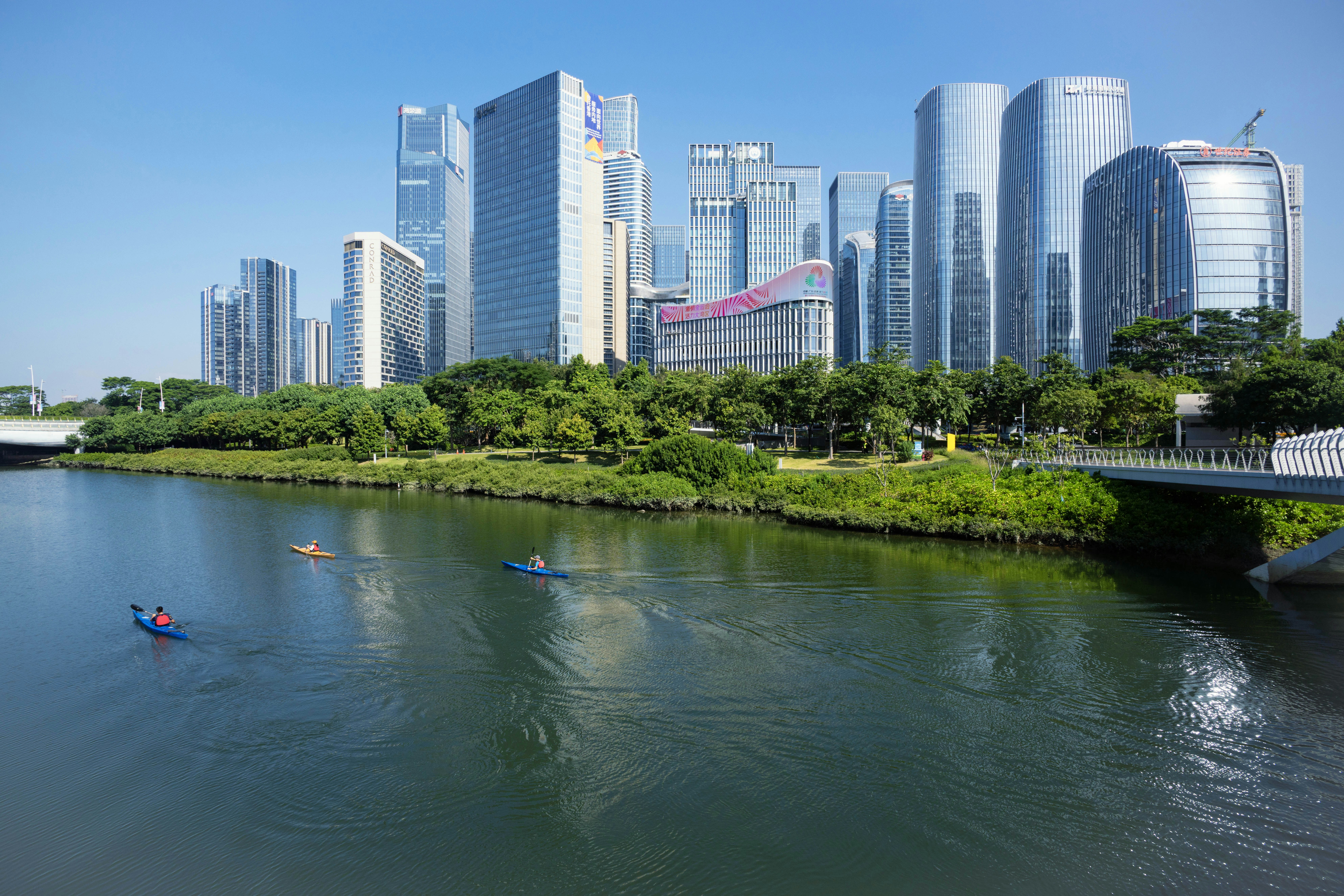 Kayakers paddle on a river with a cityscape background.