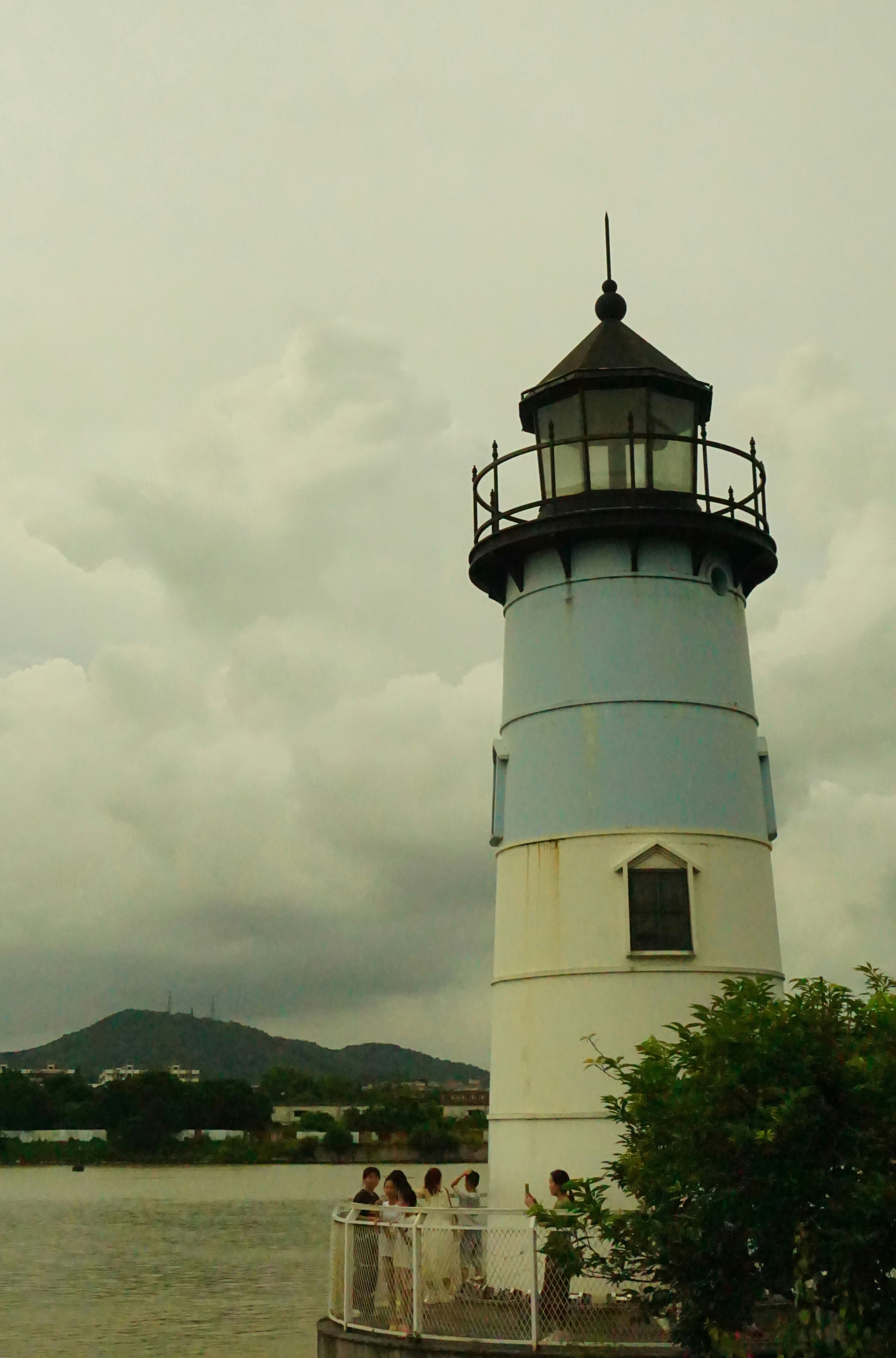 A lighthouse stands tall by the water with people.