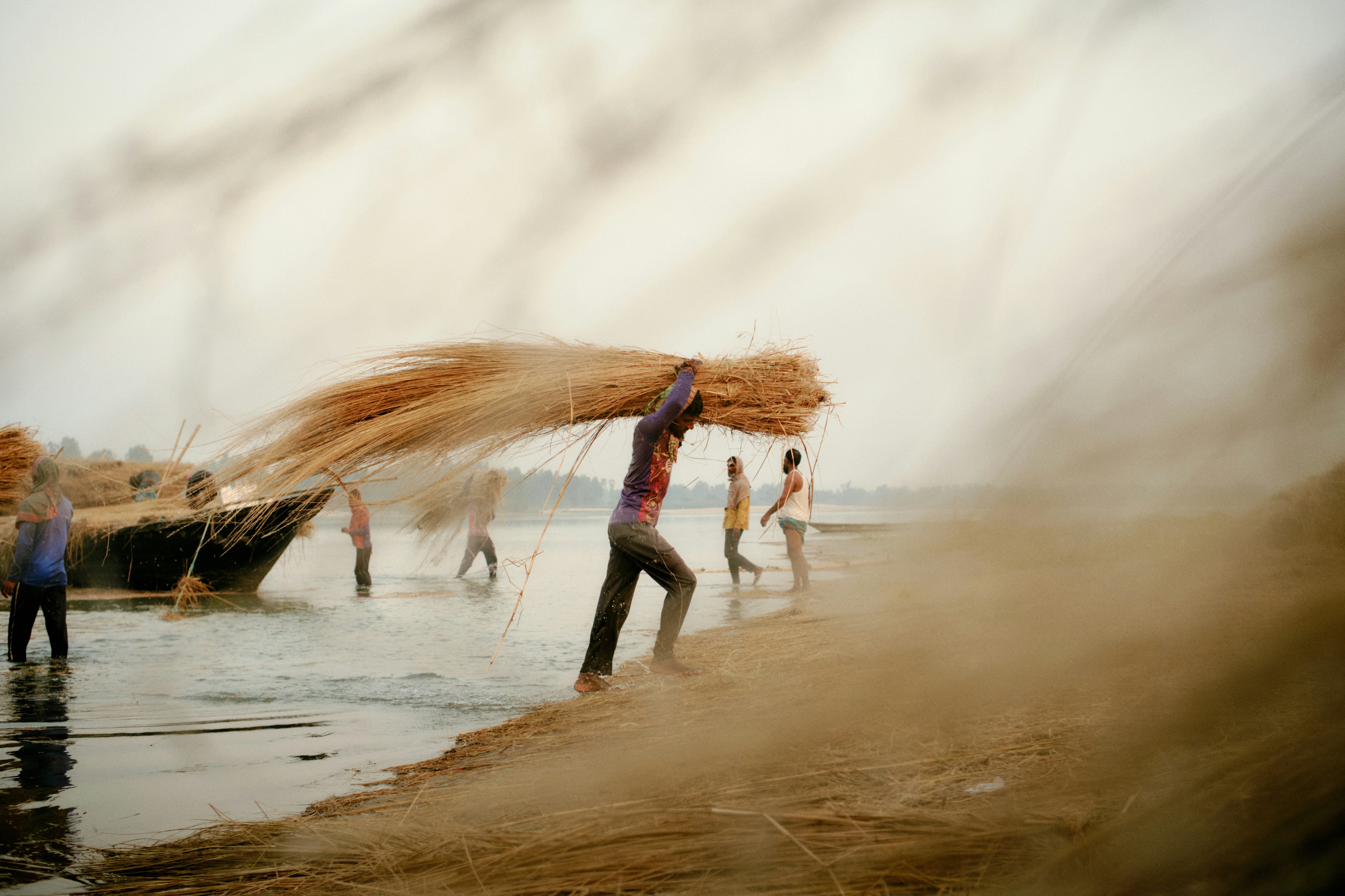 Trabalhadores descarregam palha de um barco na margem do rio.