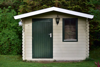A small wooden shed with a green door and window.