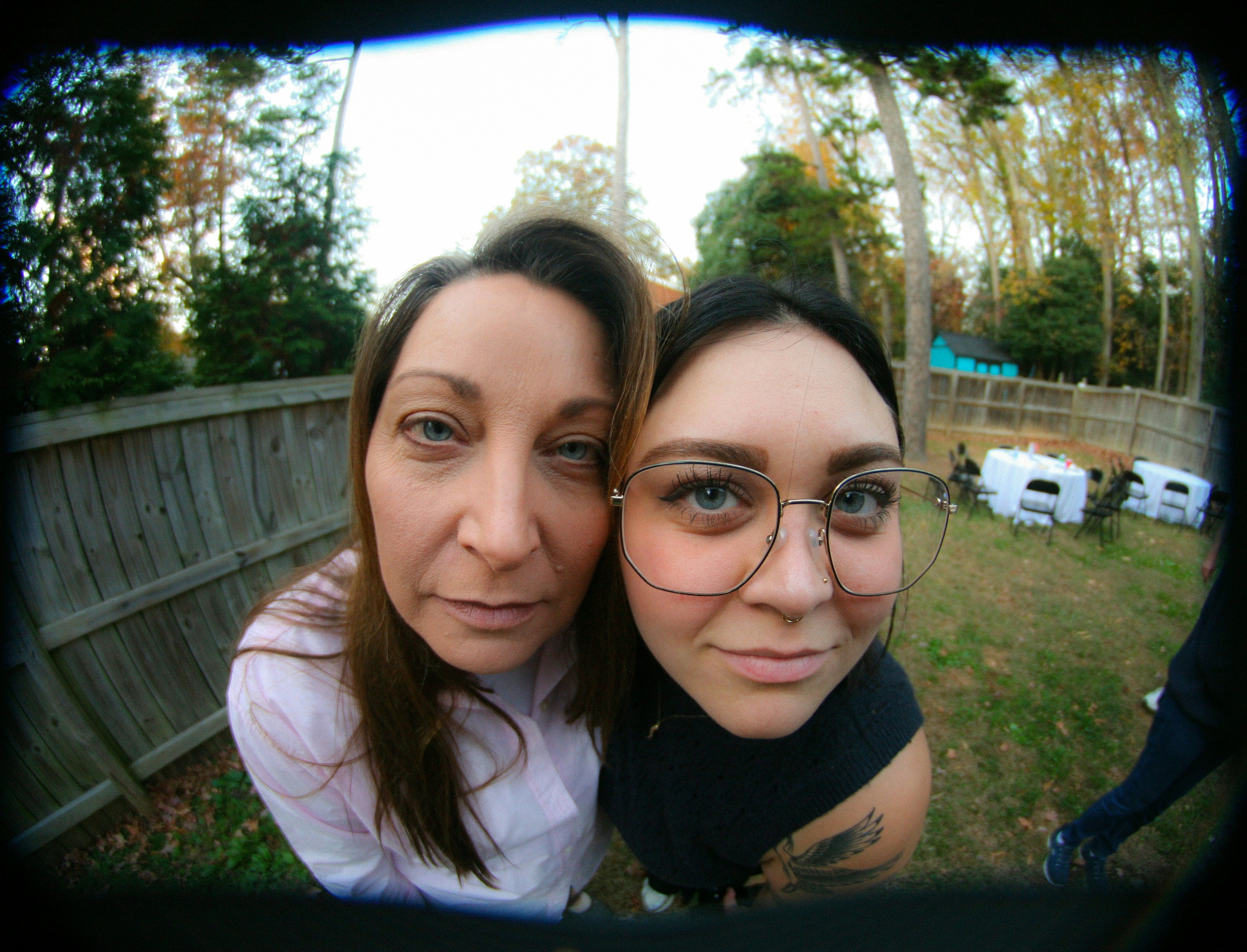 Two women pose for a fisheye lens in a backyard.