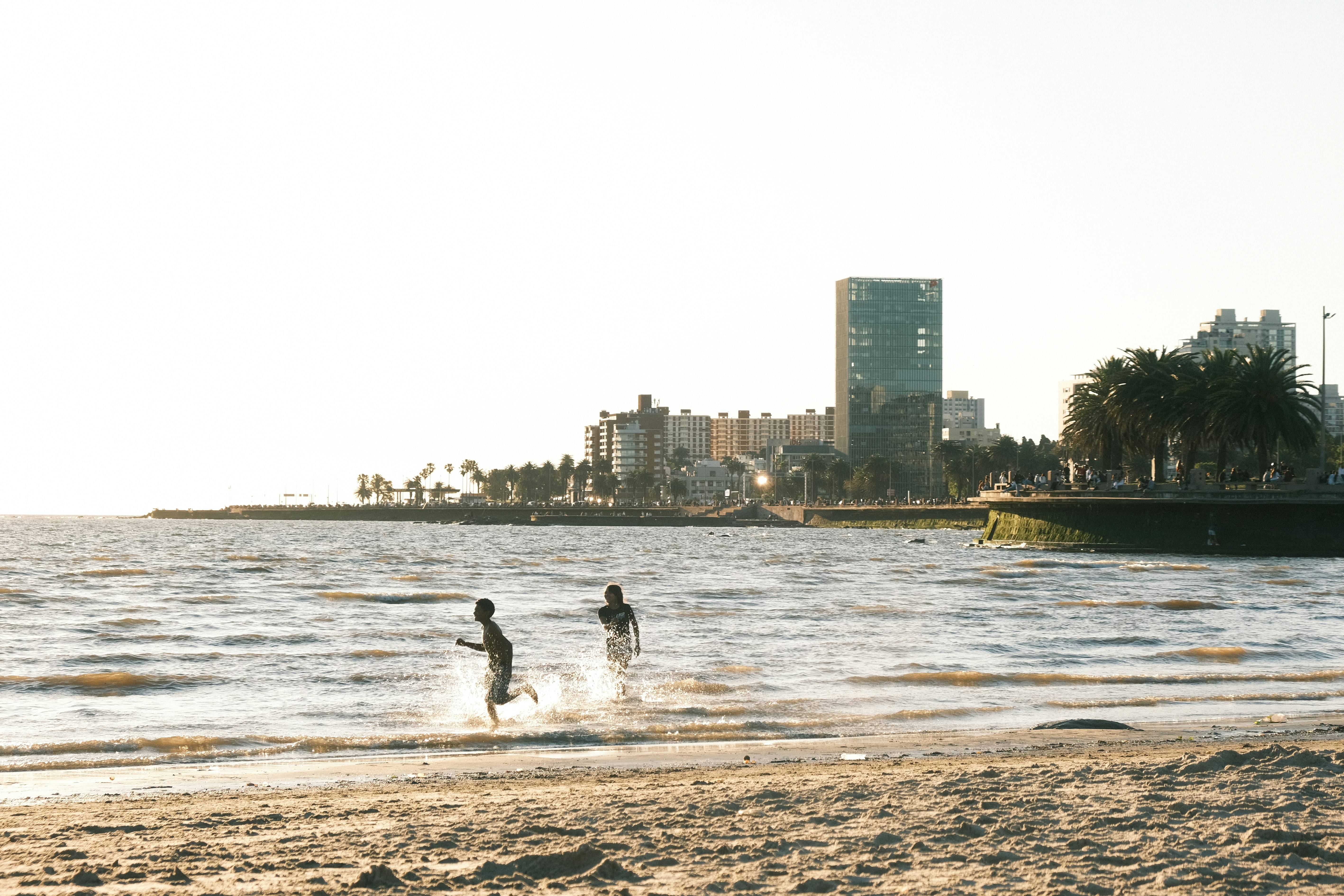 Two children run into the ocean with city skyline.