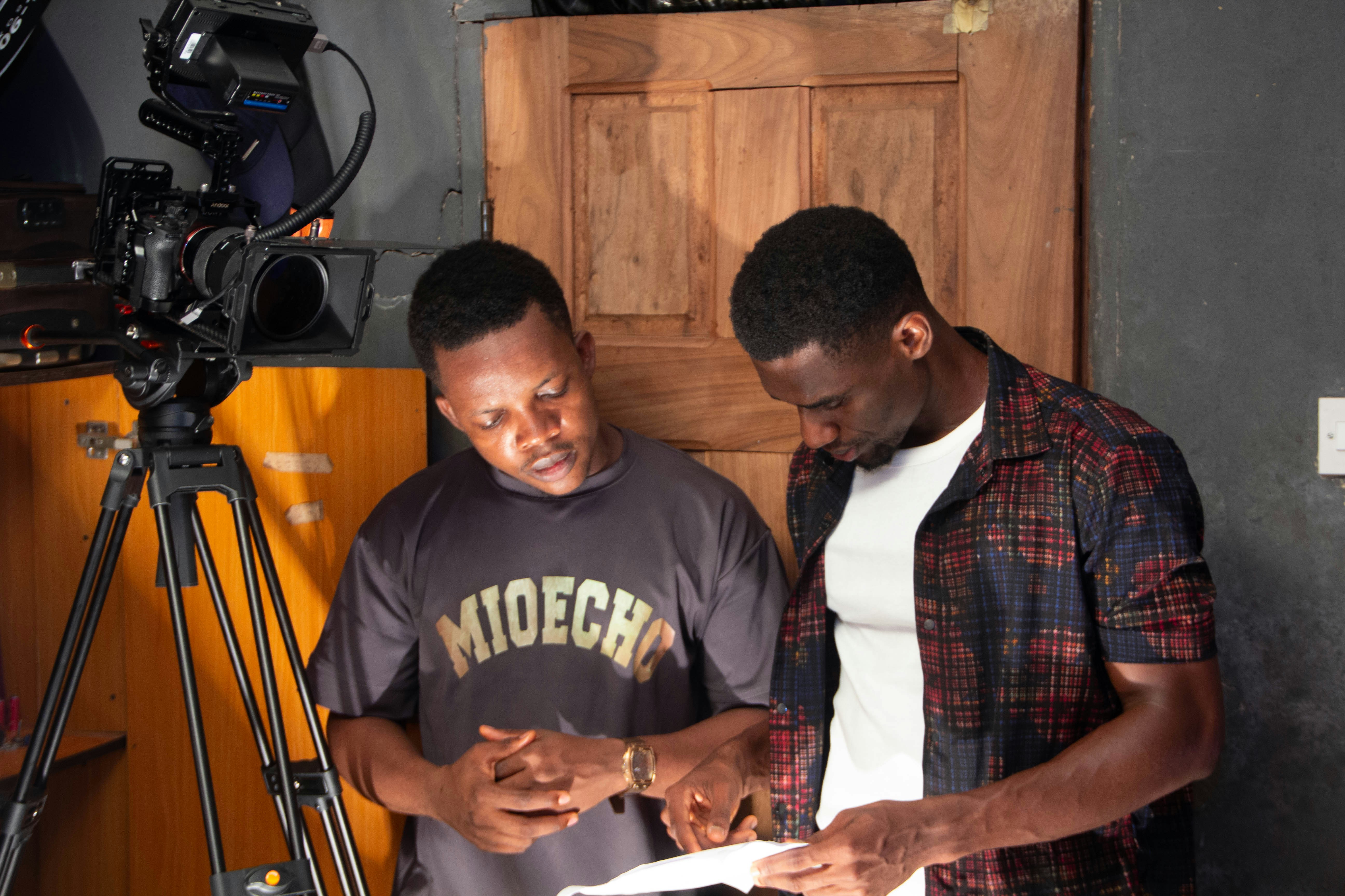 Two men looking at a script by a camera.