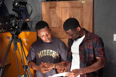 Two men looking at a script by a camera.