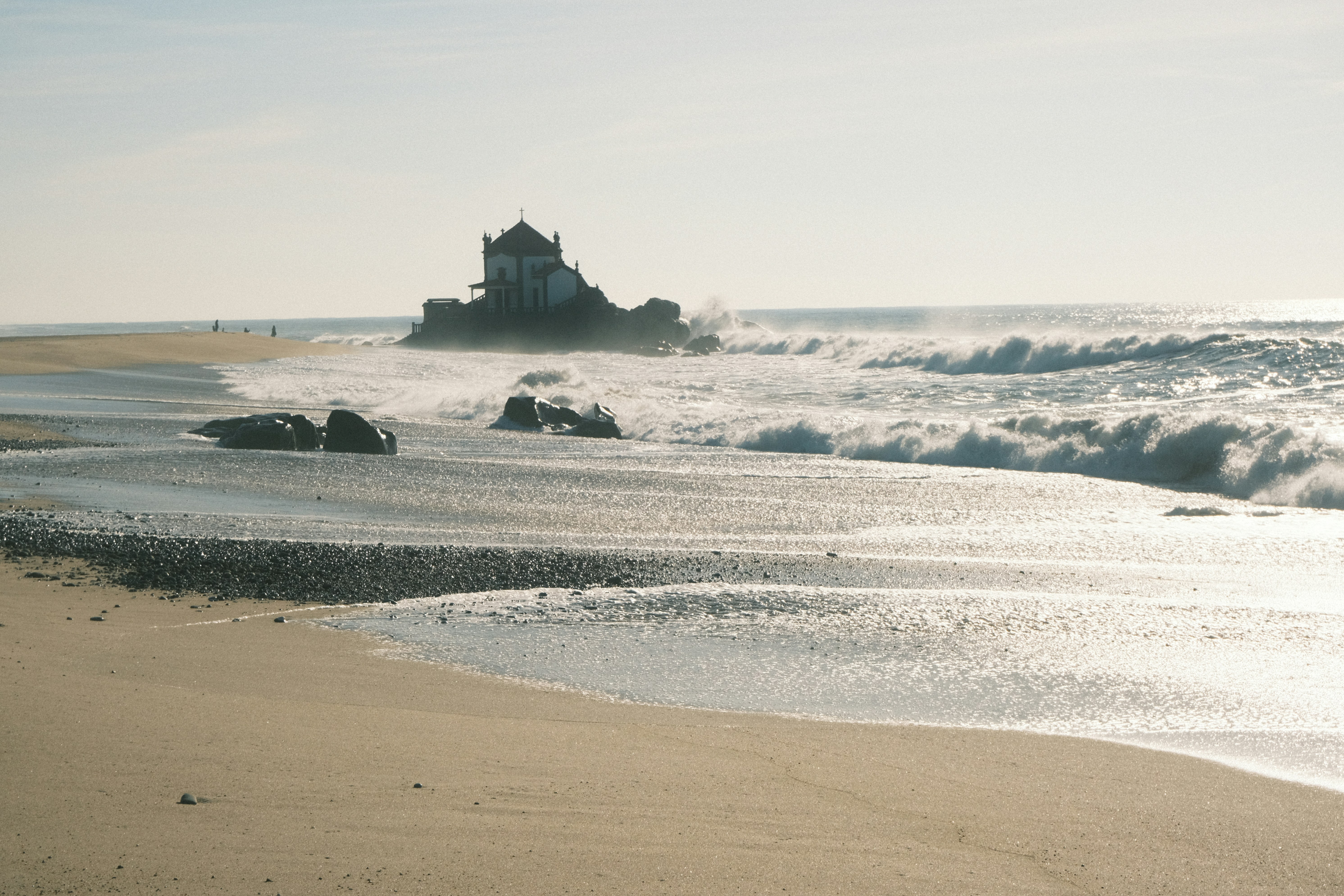 Waves crash on a rocky shore near a building.