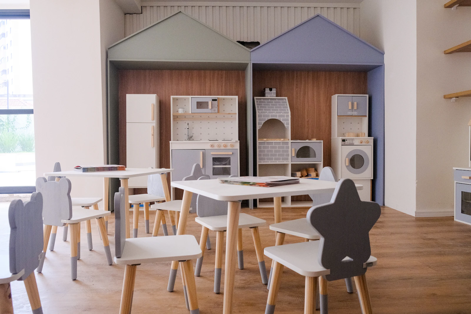 Small white tables and animal-backed chairs in a bright playroom with a wooden play kitchen