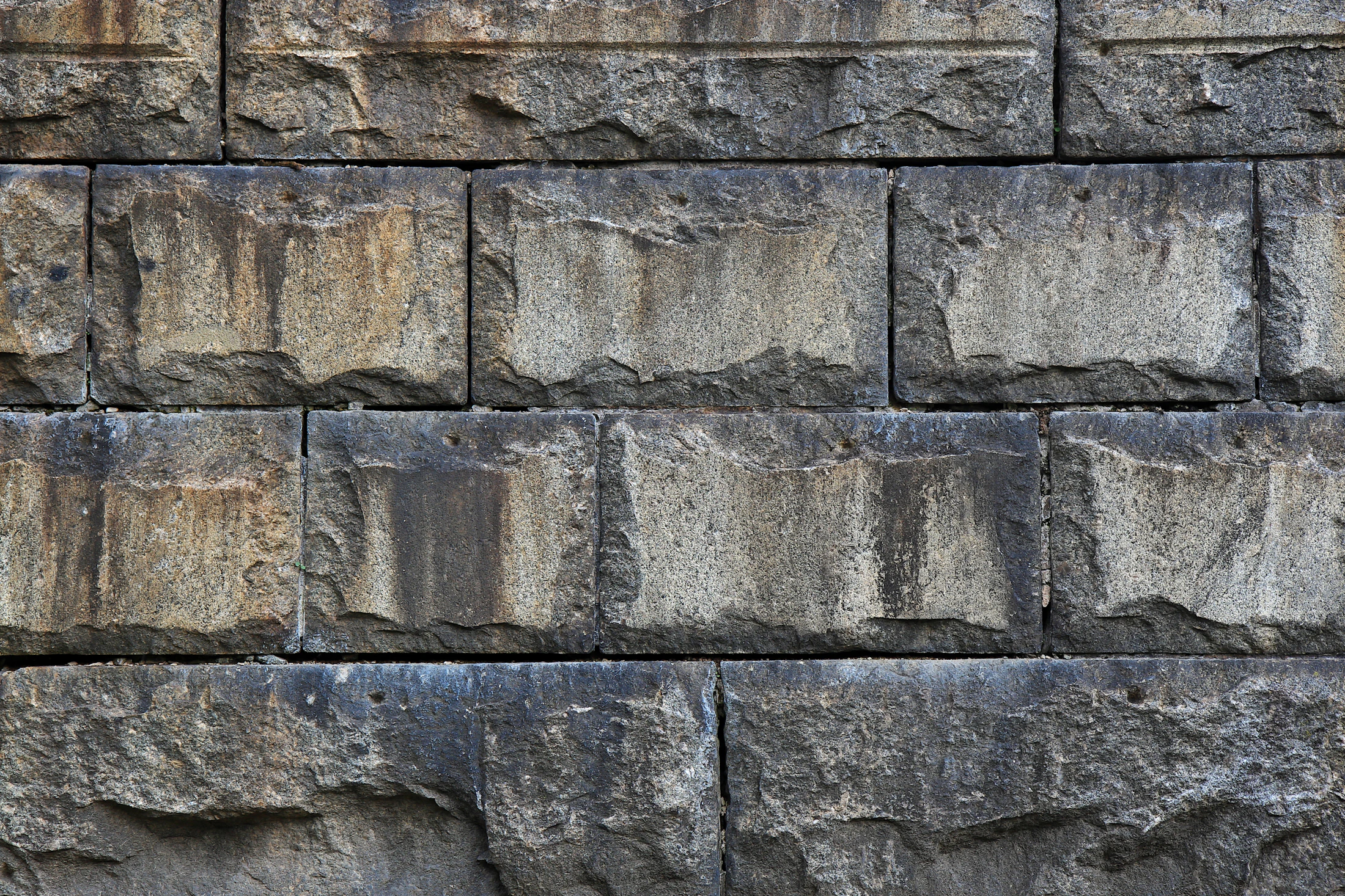 Weathered natural stone wall with dark grime and mineral streaking before restoration