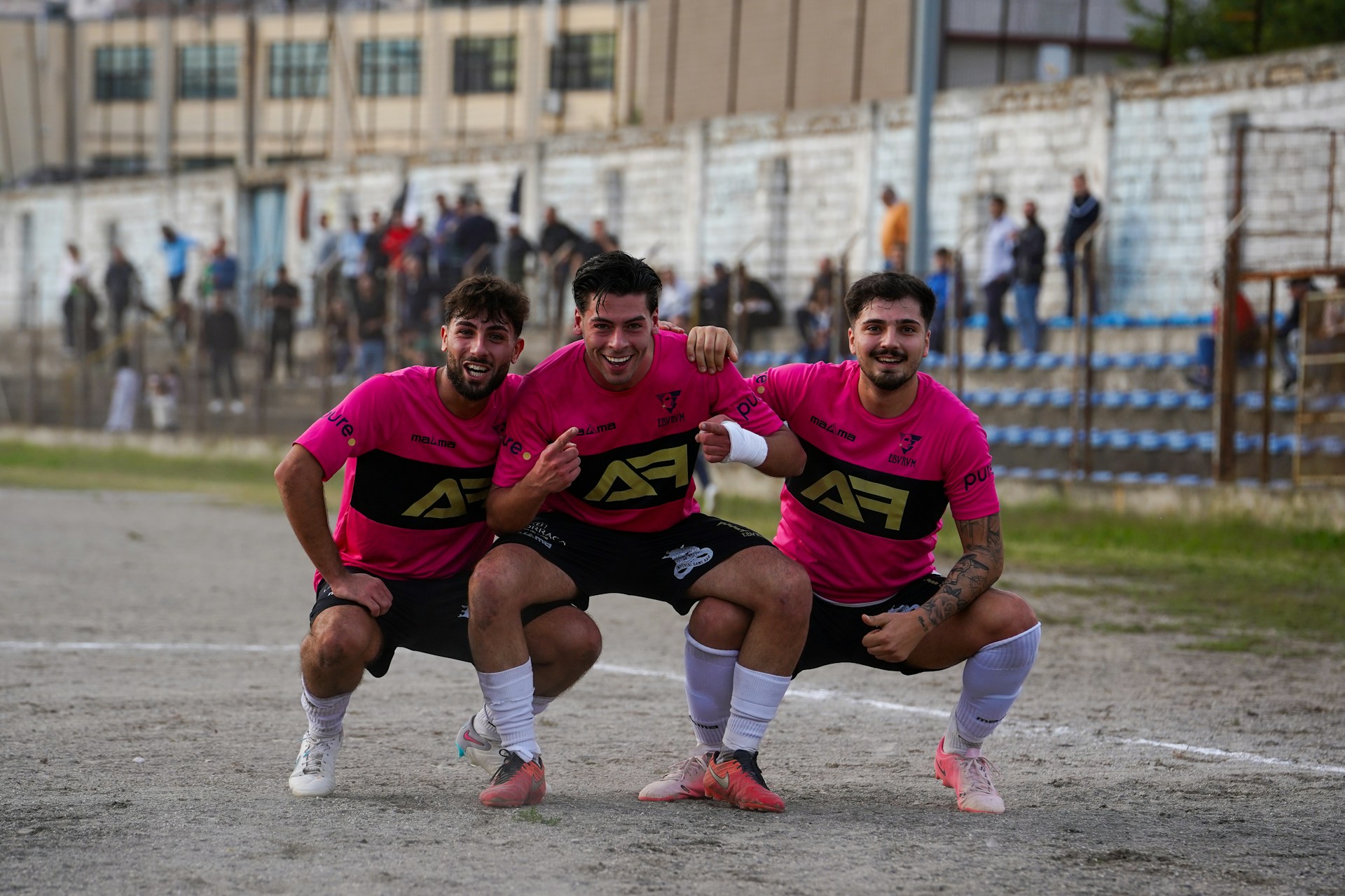 Three smiling soccer players in pink jerseys celebrating