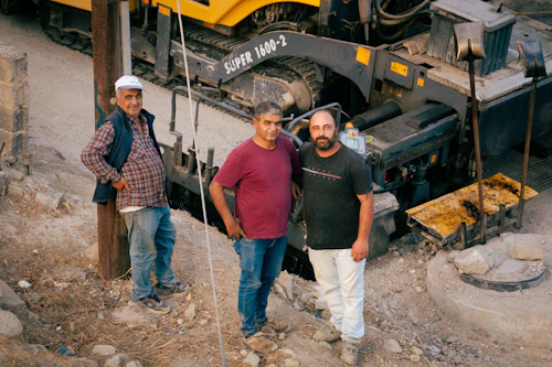 Three construction workers standing beside heavy paving equipment