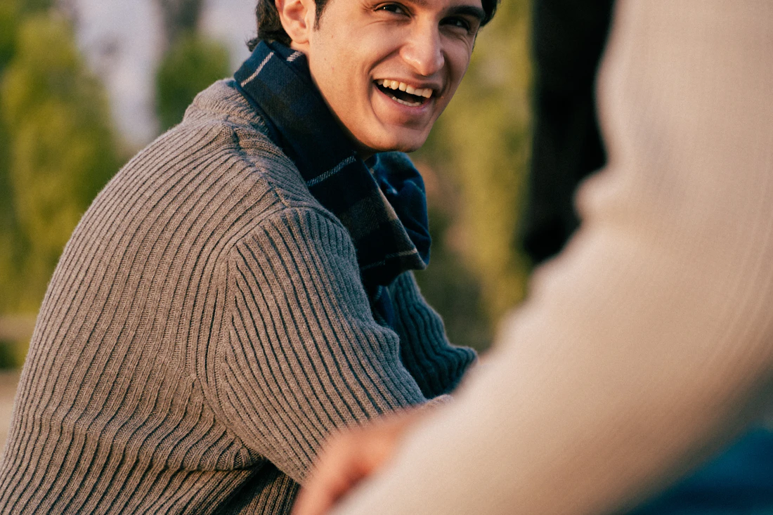 A young man in a grey sweater laughing outdoors
