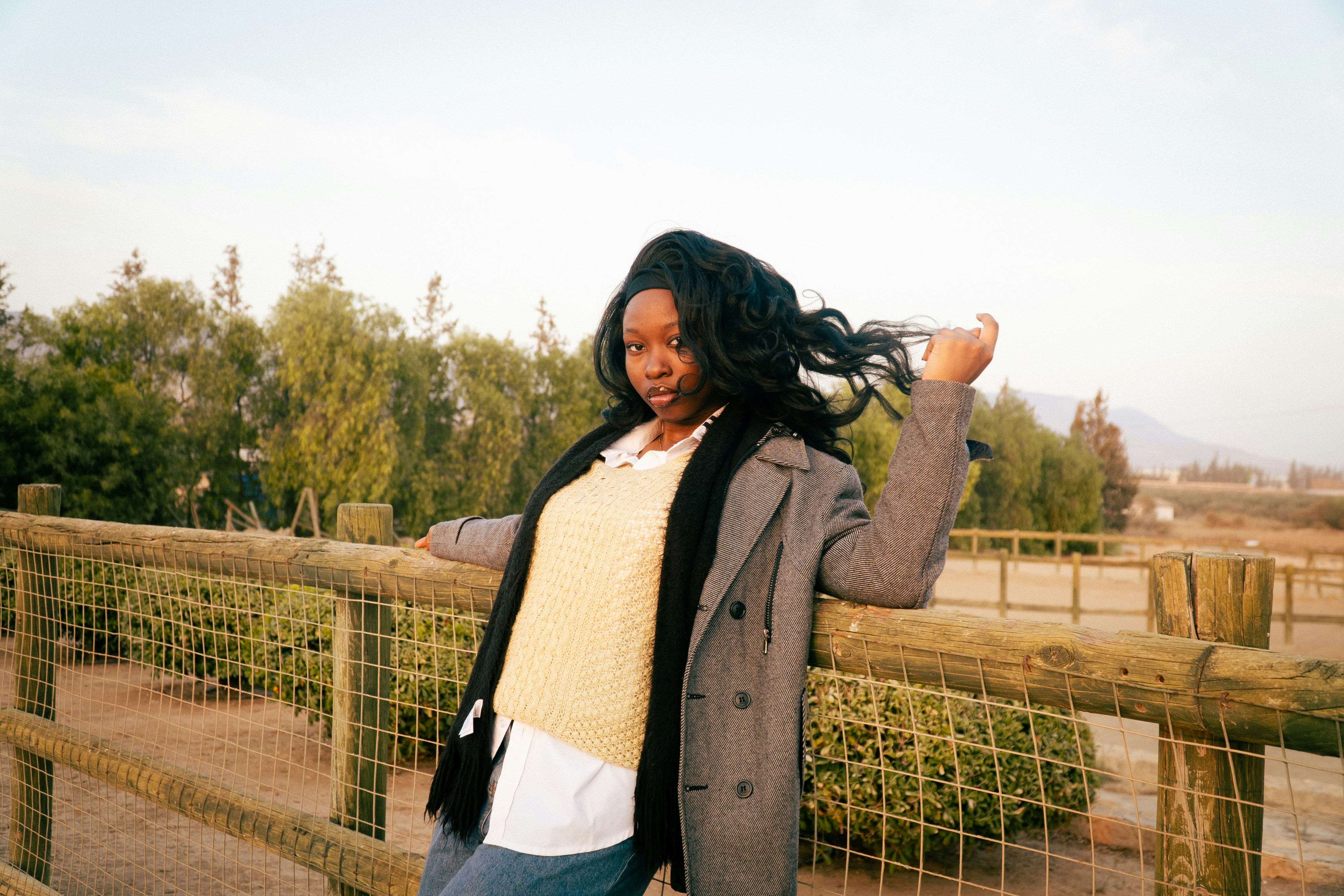 Young woman with long dark hair leaning on fence.