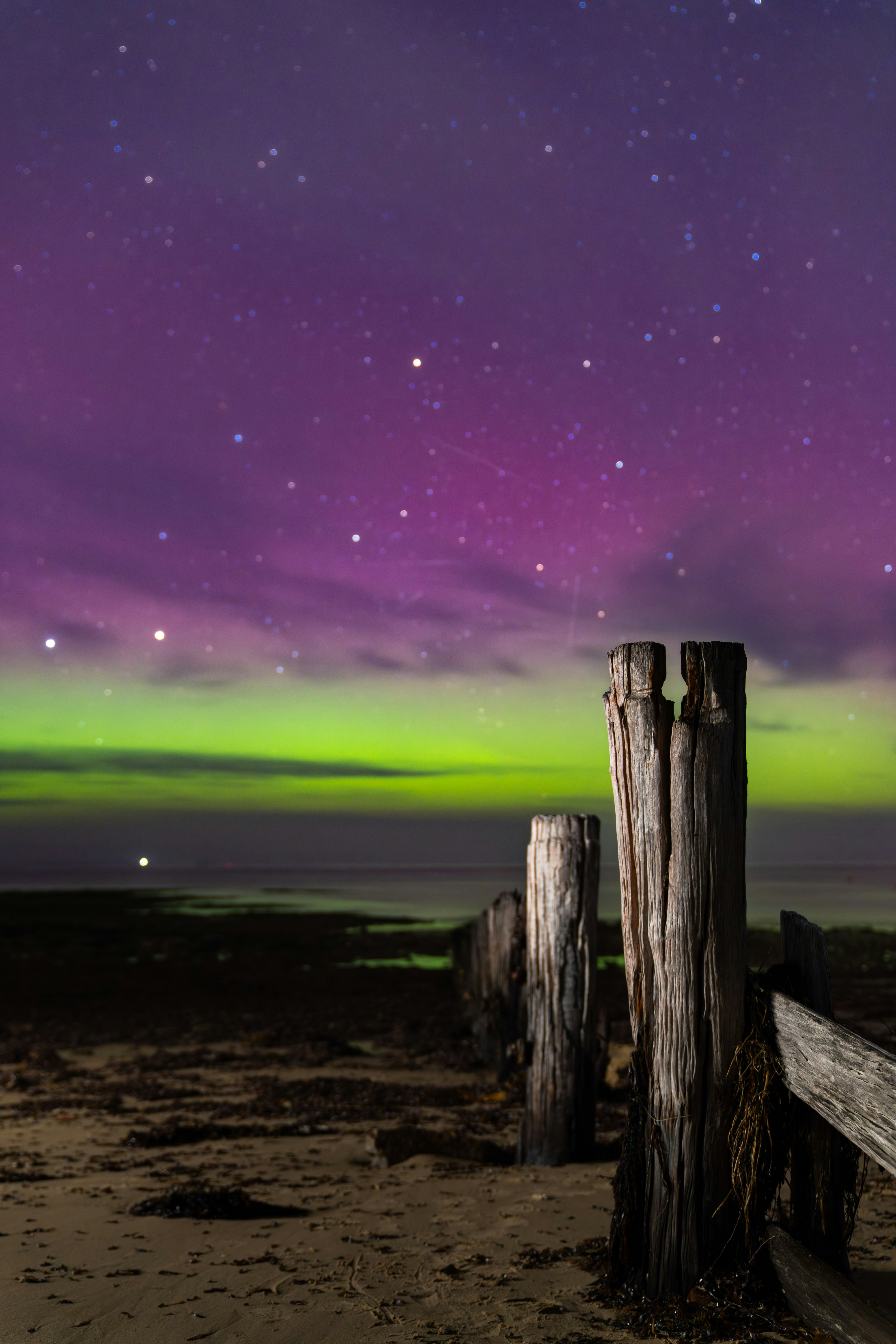 Aurore boréale au-dessus d’une plage avec des poteaux en bois.