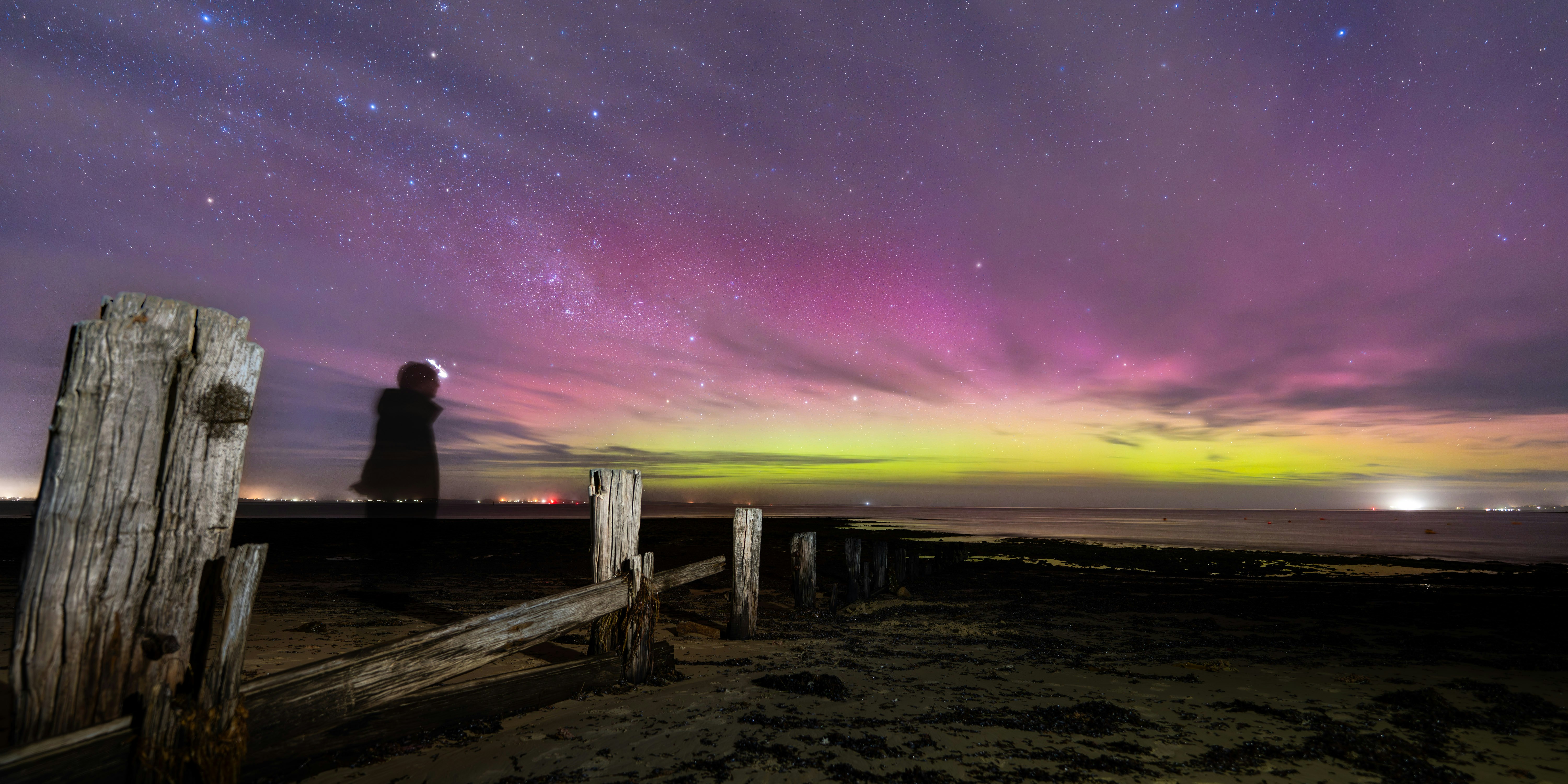 La personne observe l’aurore boréale au-dessus de l’océan la nuit.