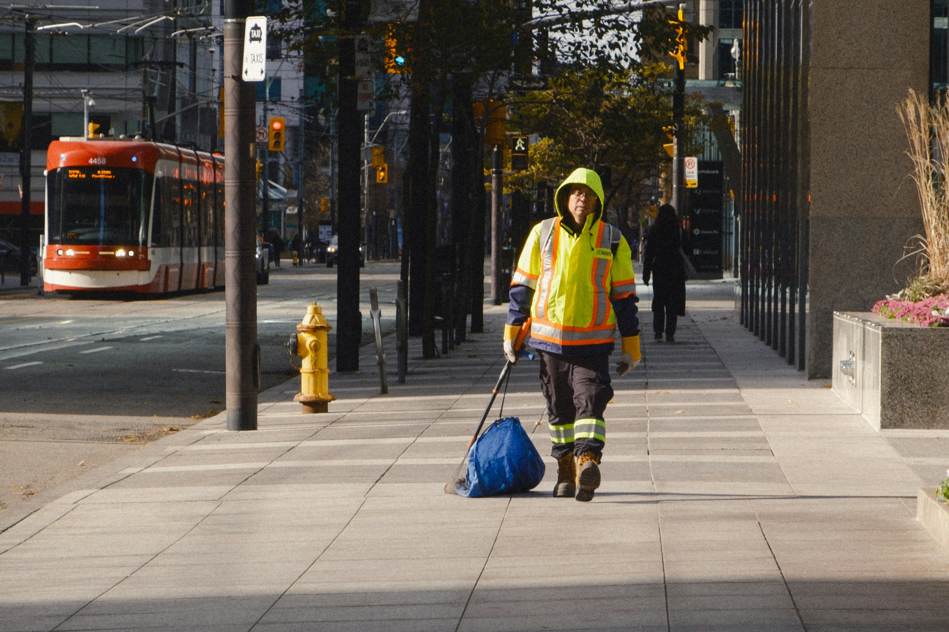Worker in reflective gear walks down city sidewalk