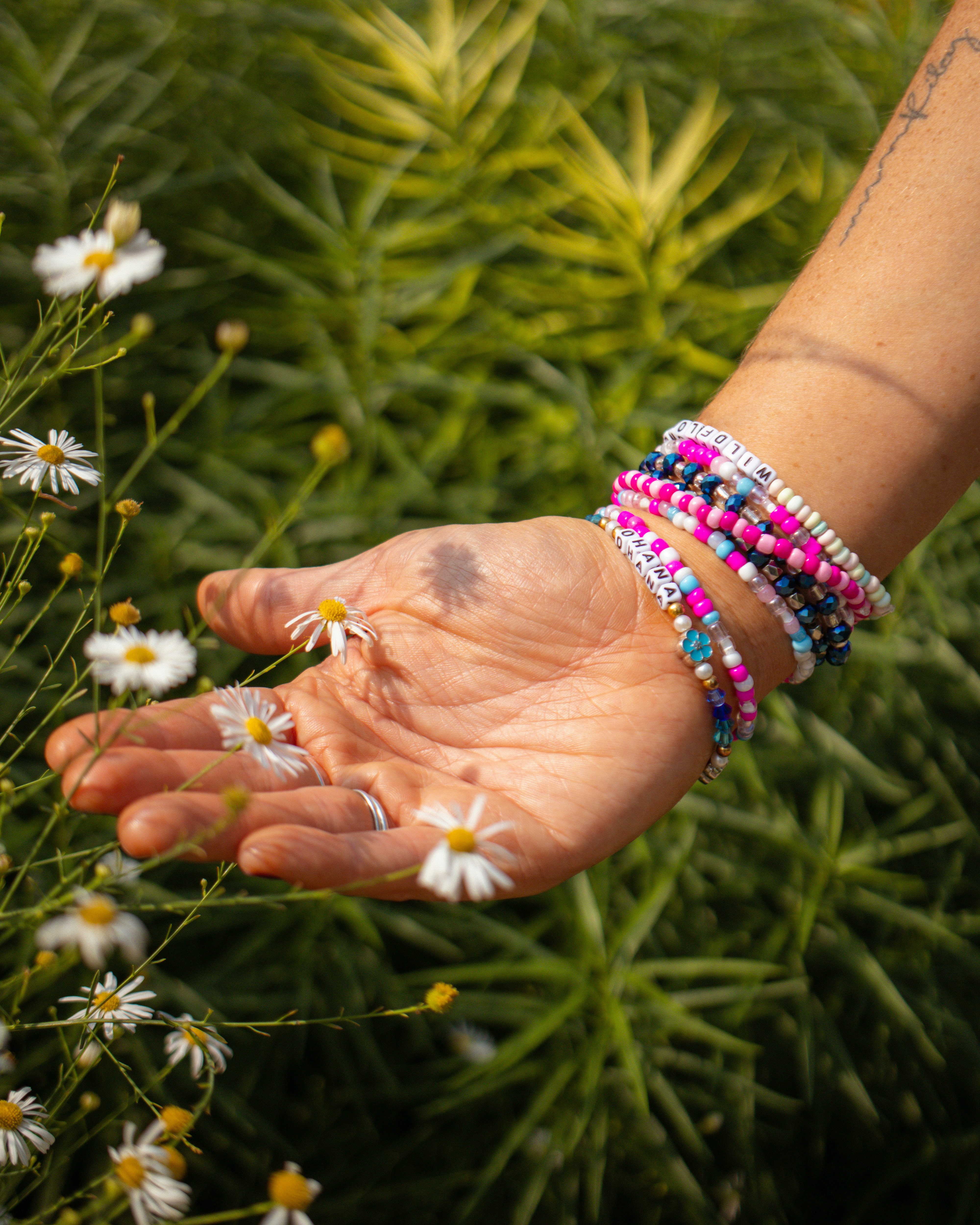 Hand wearing bracelets touches small white flowers