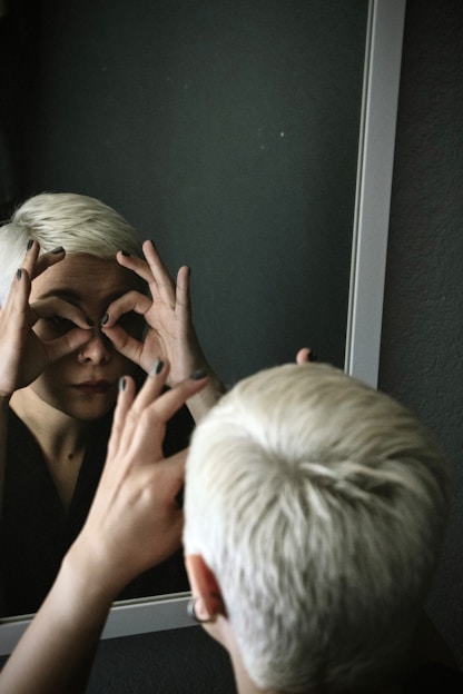 Woman looking through fingers in mirror
