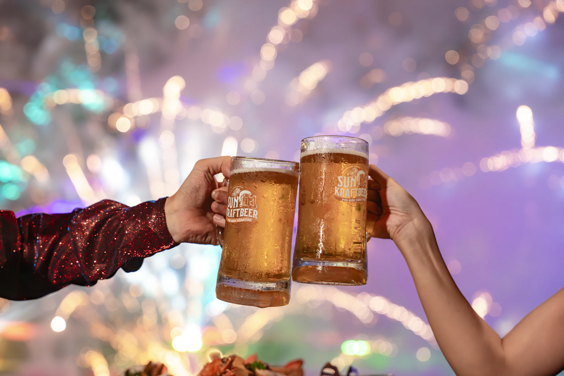 Two hands clinking beer mugs with fireworks behind.