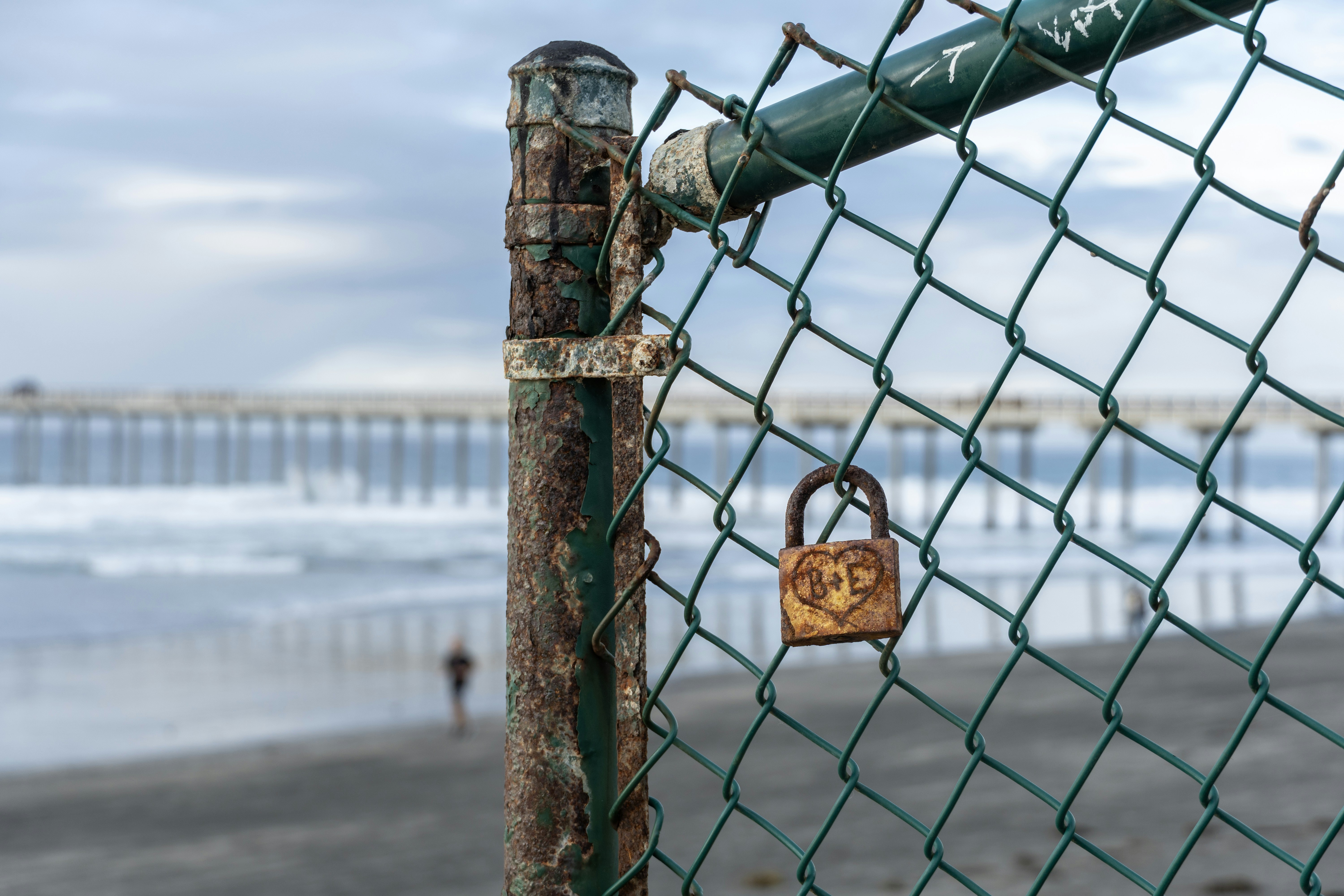 Rusty padlock on chain-link fence at beach