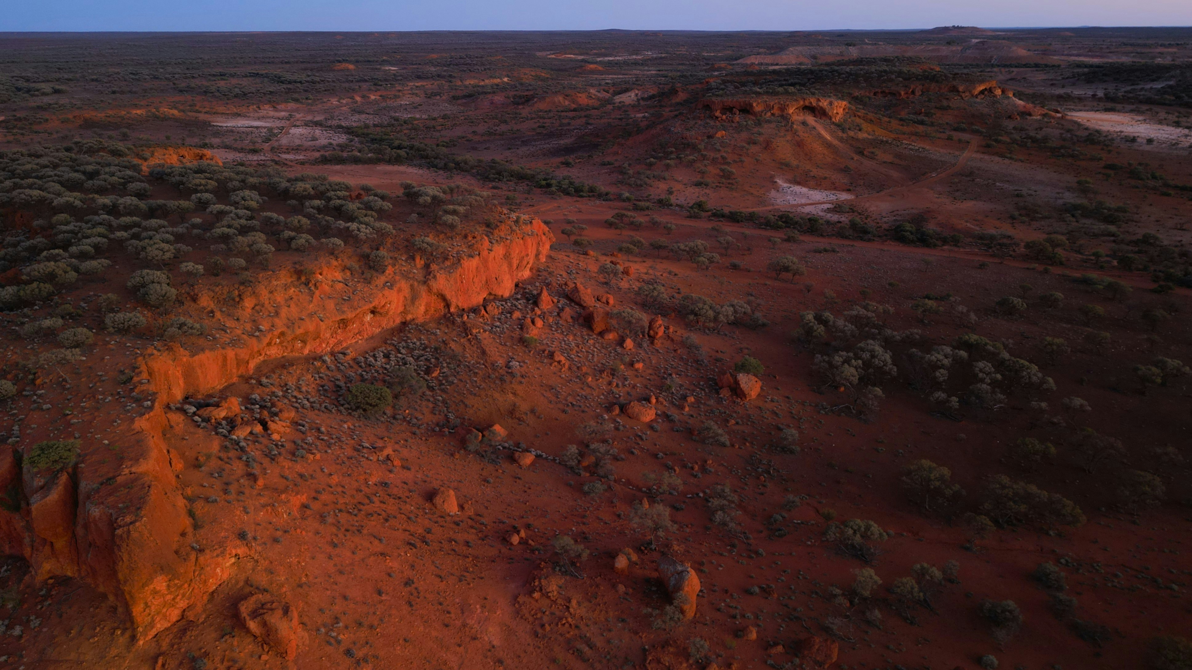 Vast desert landscape at dusk with red rock formations.