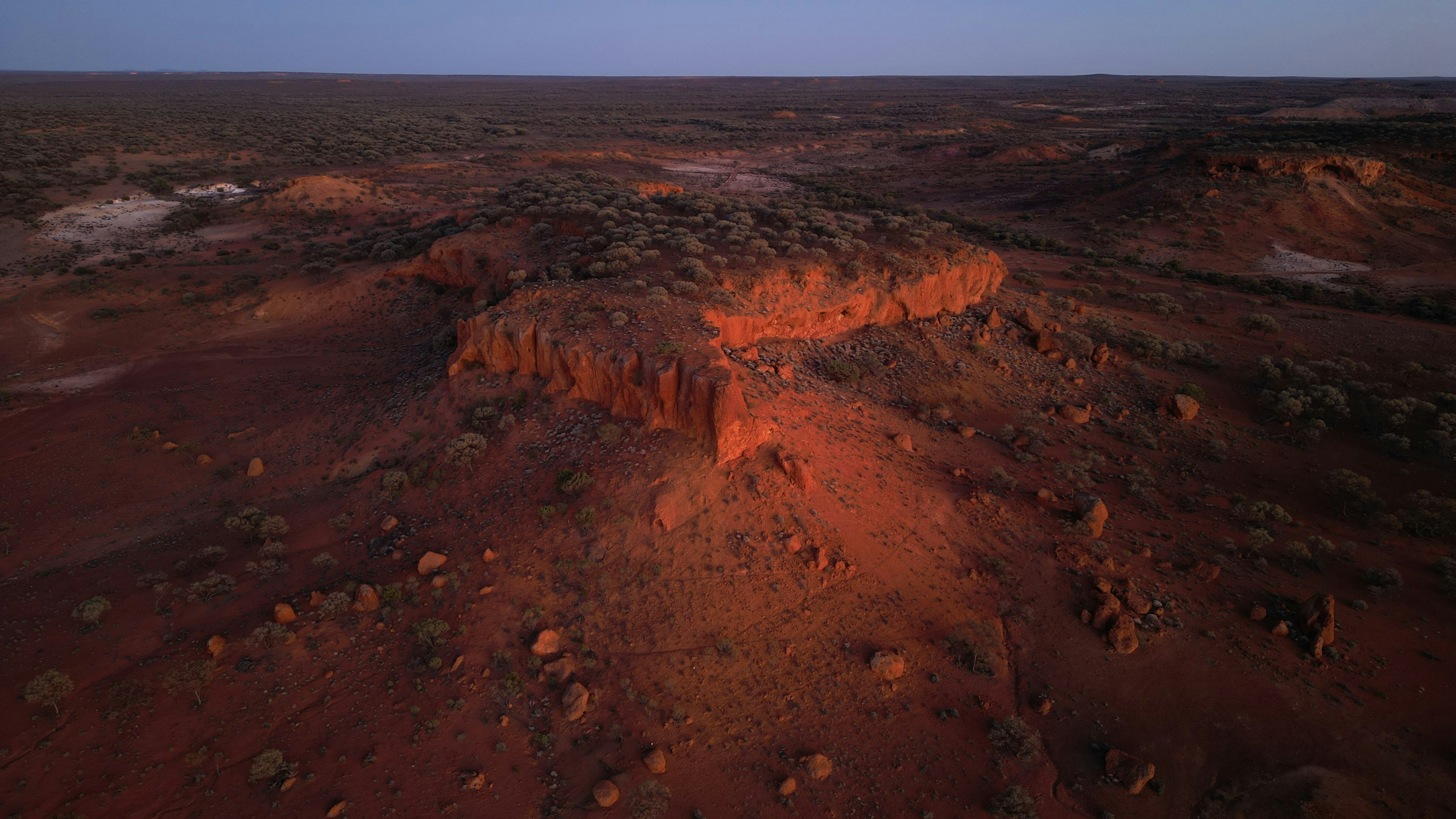 Red desert landscape at sunset with low vegetation.