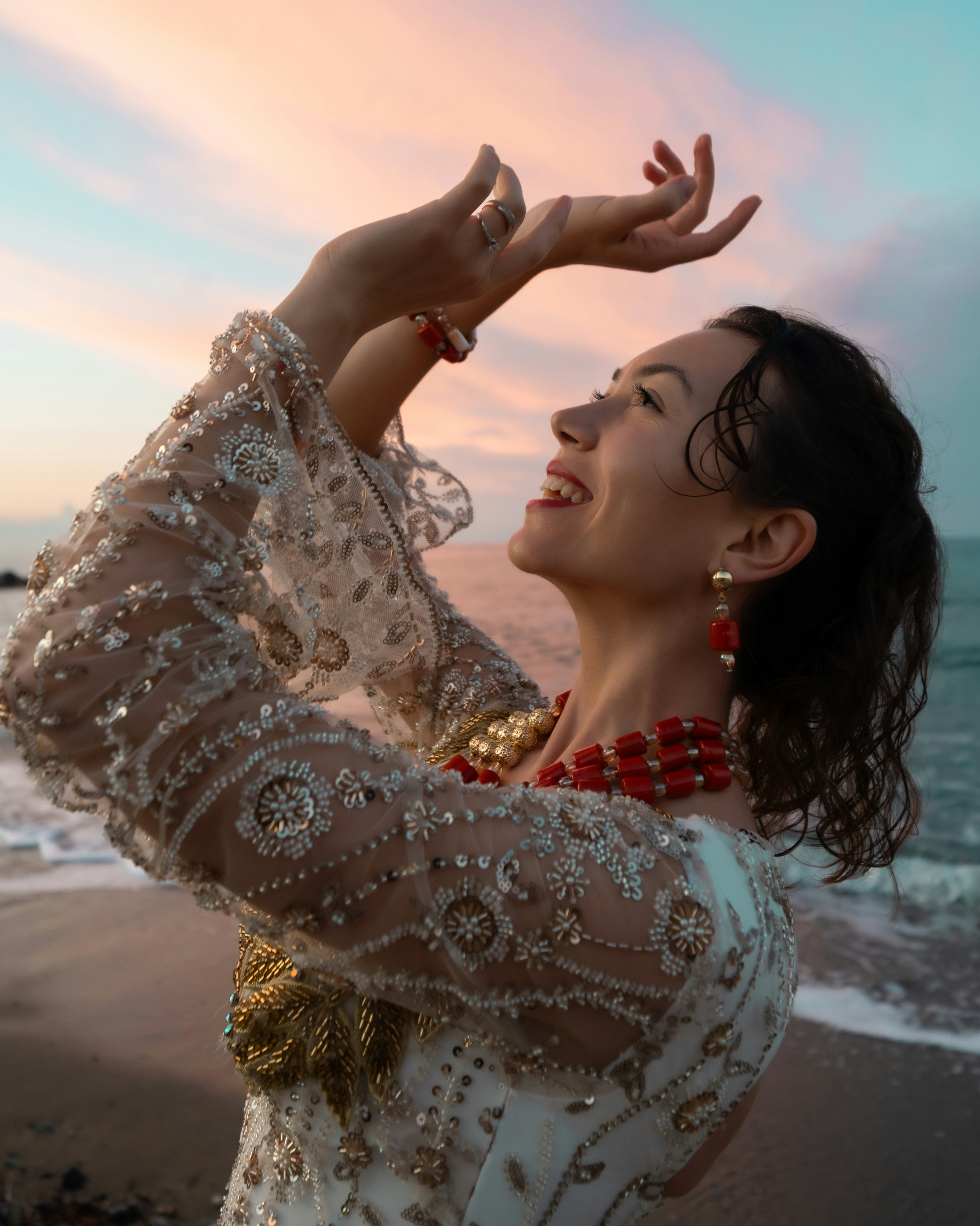 Mujer con vestido ornamentado bailando en la playa al atardecer