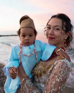 Woman holding a baby in traditional attire by the ocean