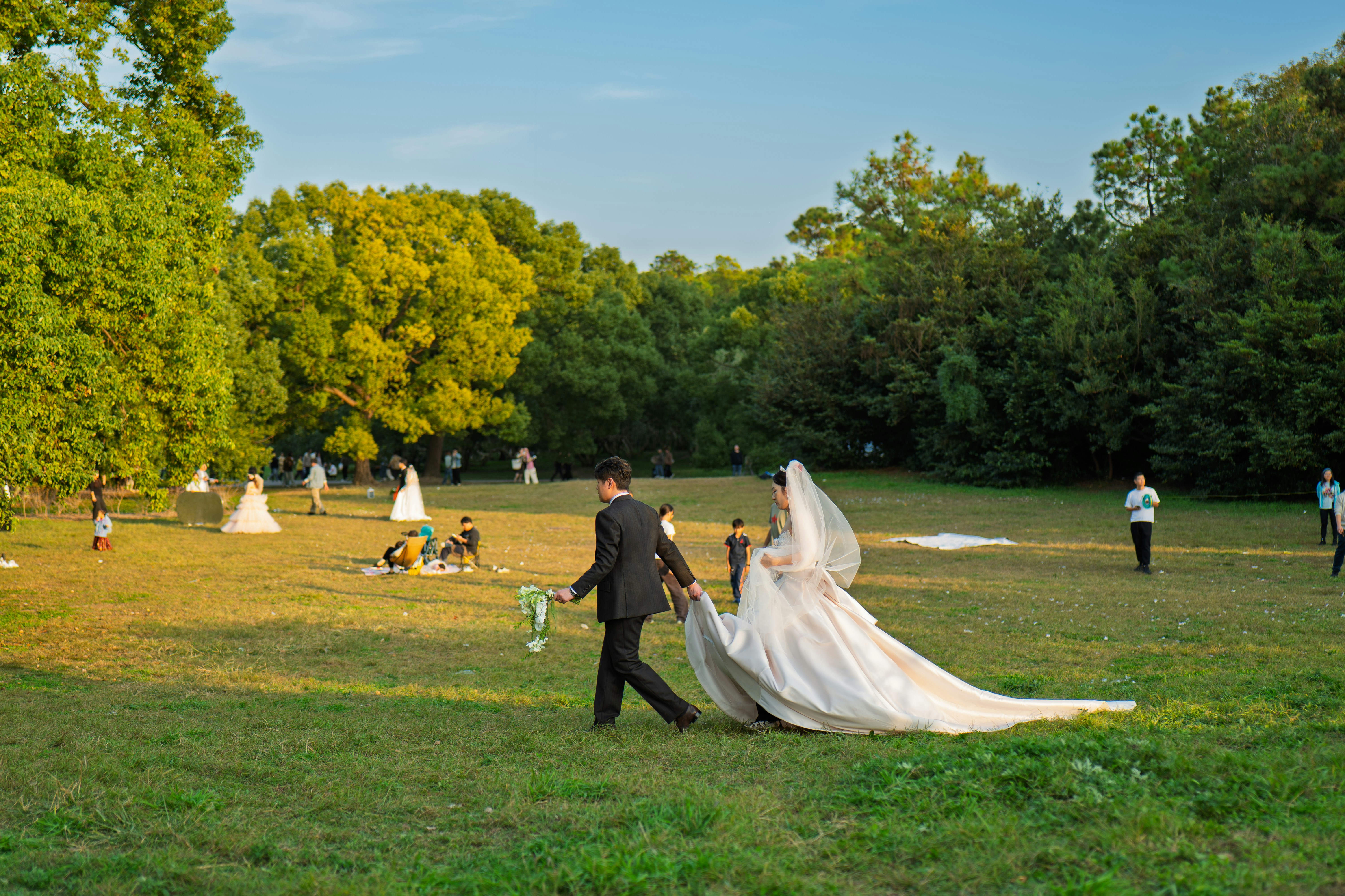 Bride and groom walking in a park with guests
