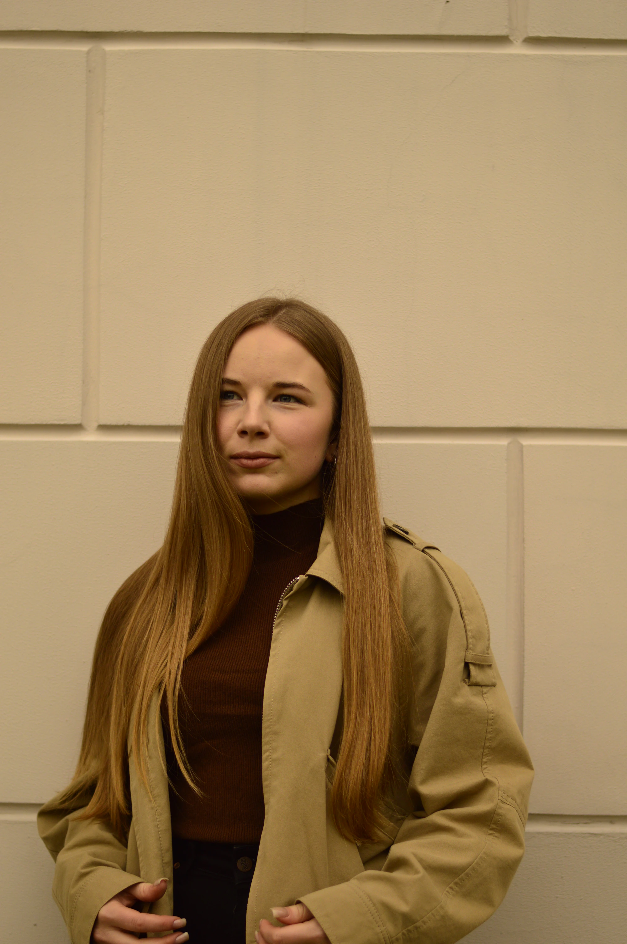 A woman in a trench coat against a beige wall