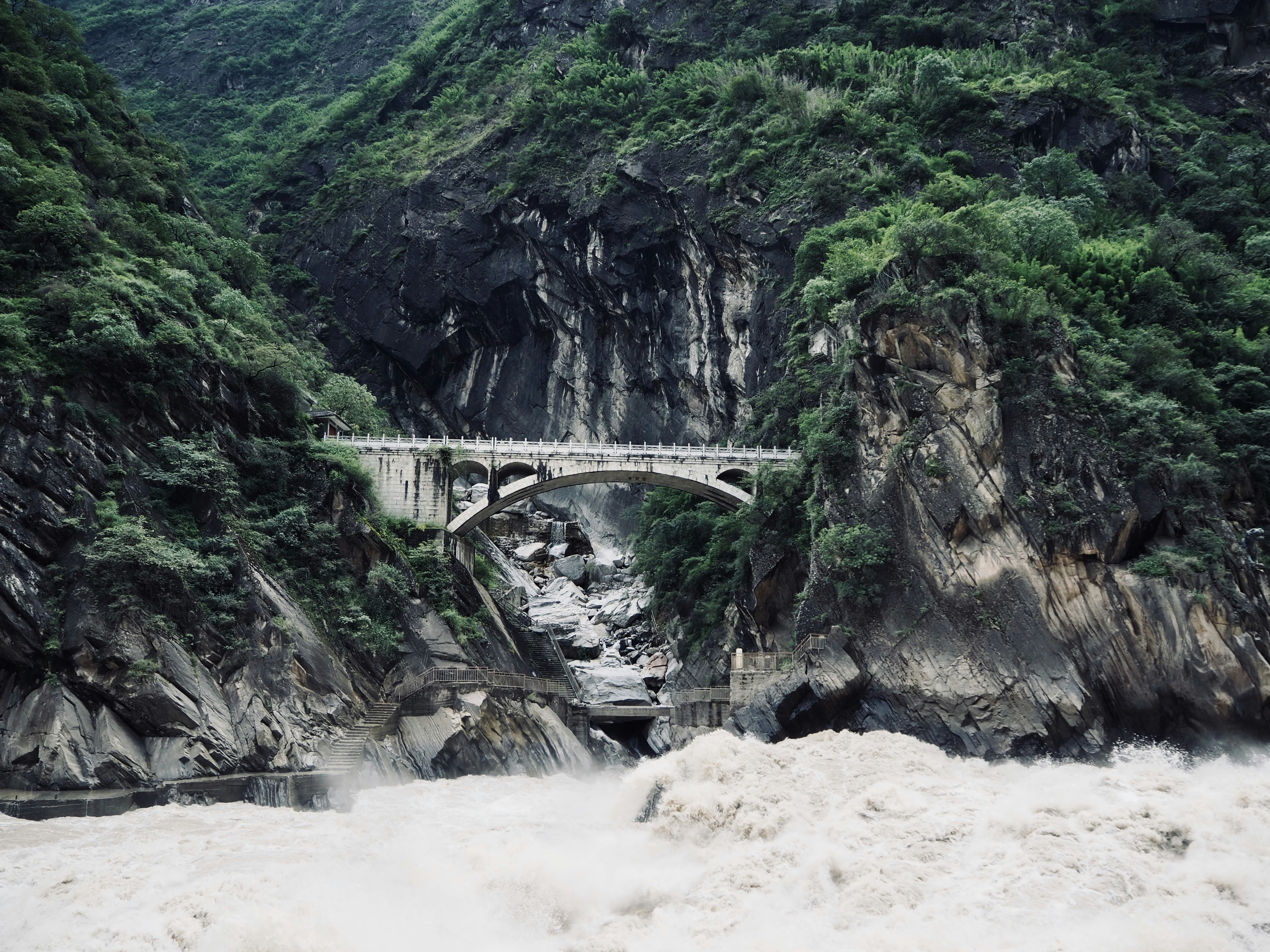 A bridge spans a turbulent river in a lush gorge.