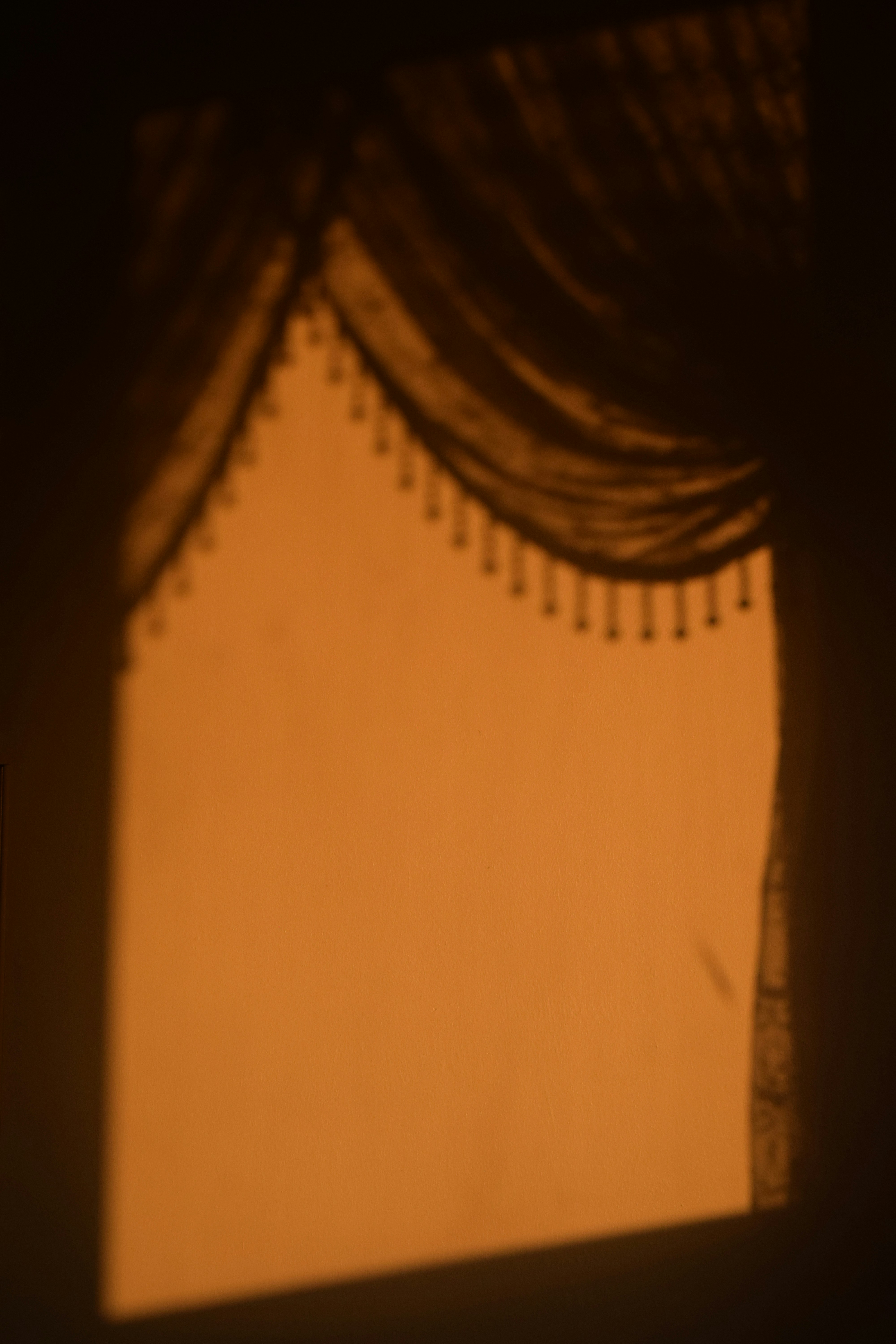 Shadows of curtains cast on an orange wall.