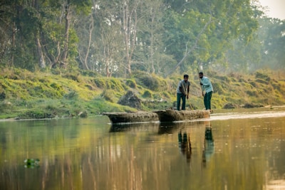 Two men standing in a small boat on a river.
