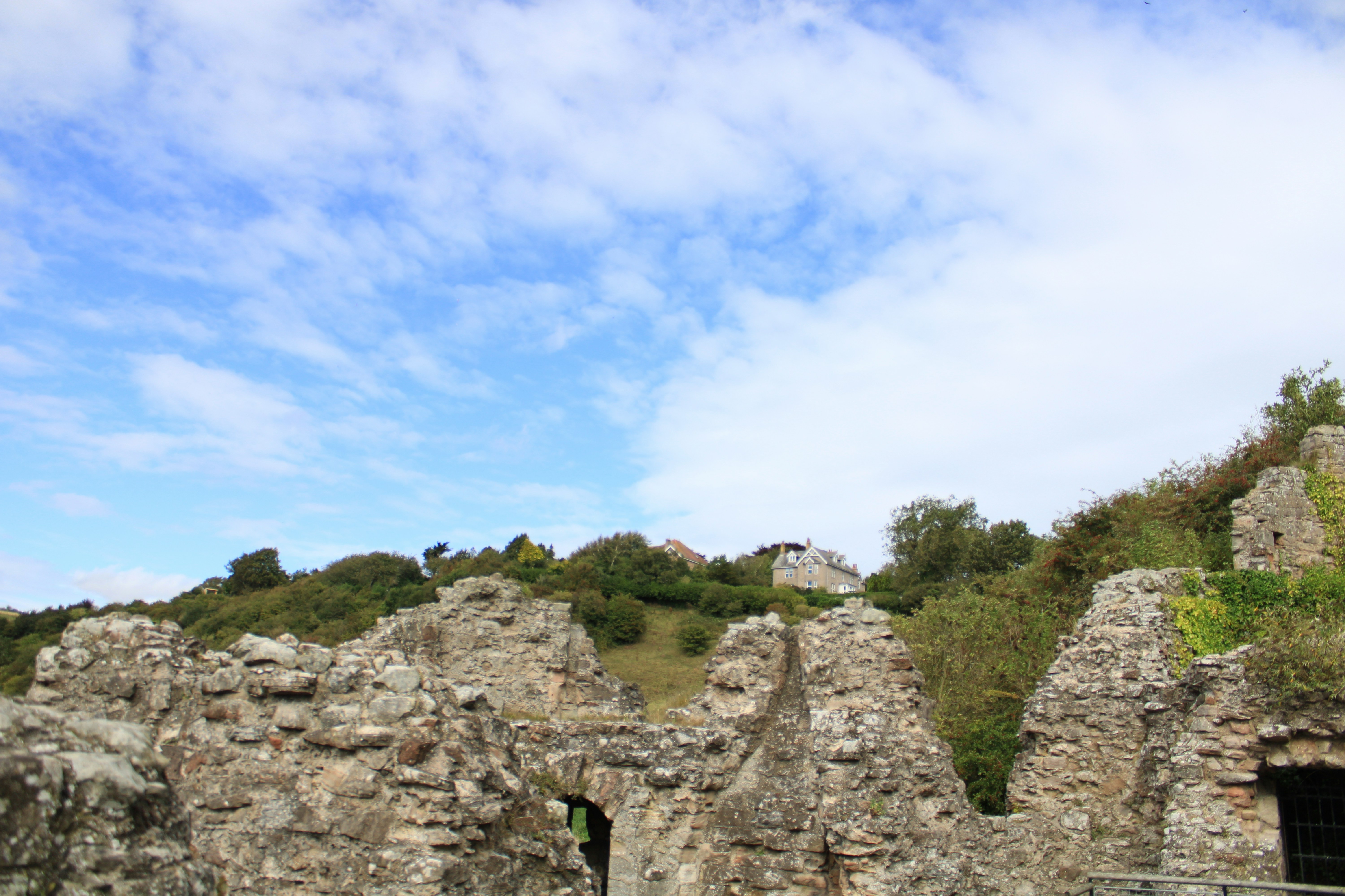 Ancient stone ruins on a grassy hillside under blue sky.