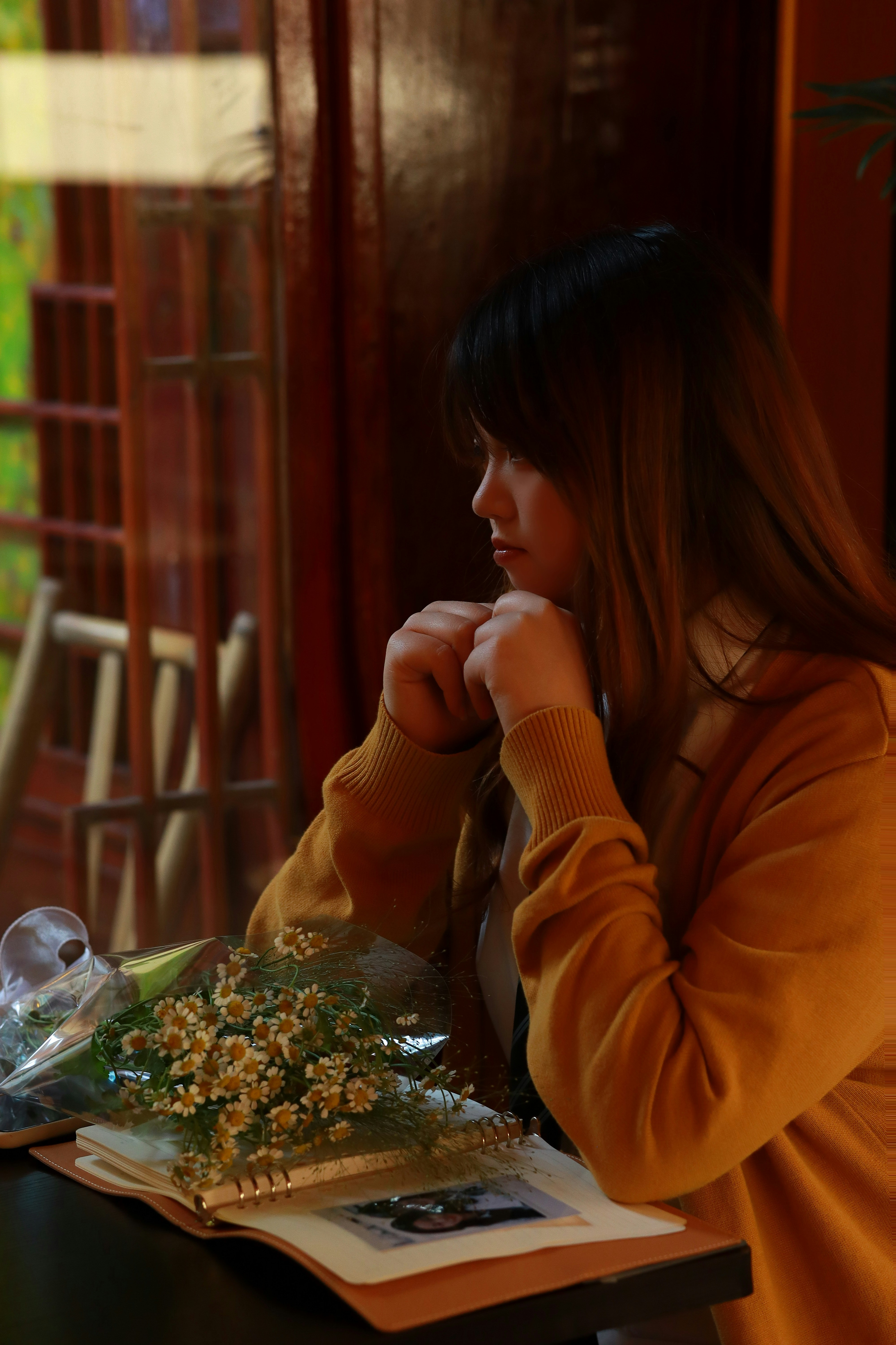 Junge Frau, die mit Blumen und einem Buch aus dem Fenster schaut.