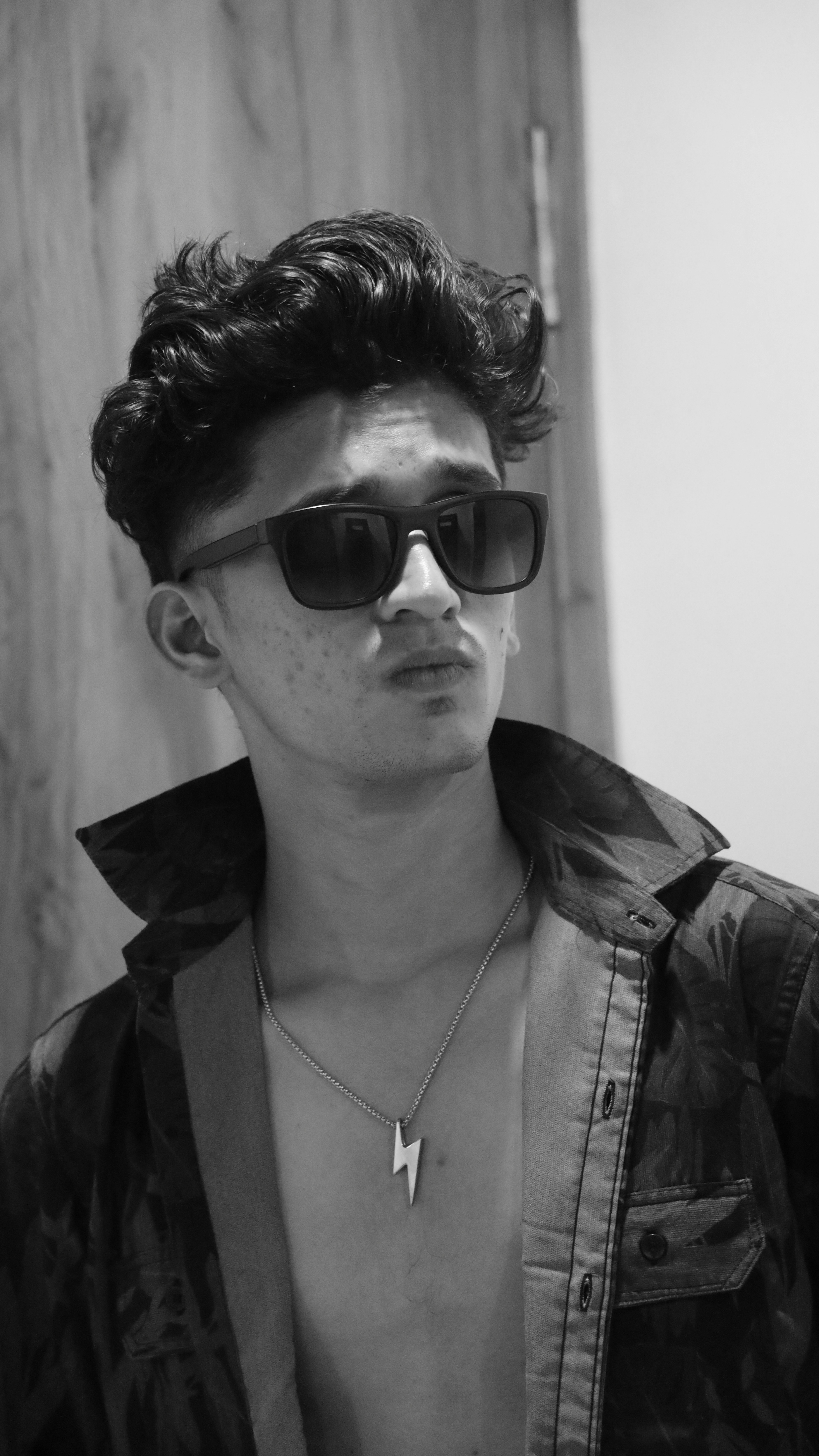 Young man wearing sunglasses and a lightning bolt necklace.