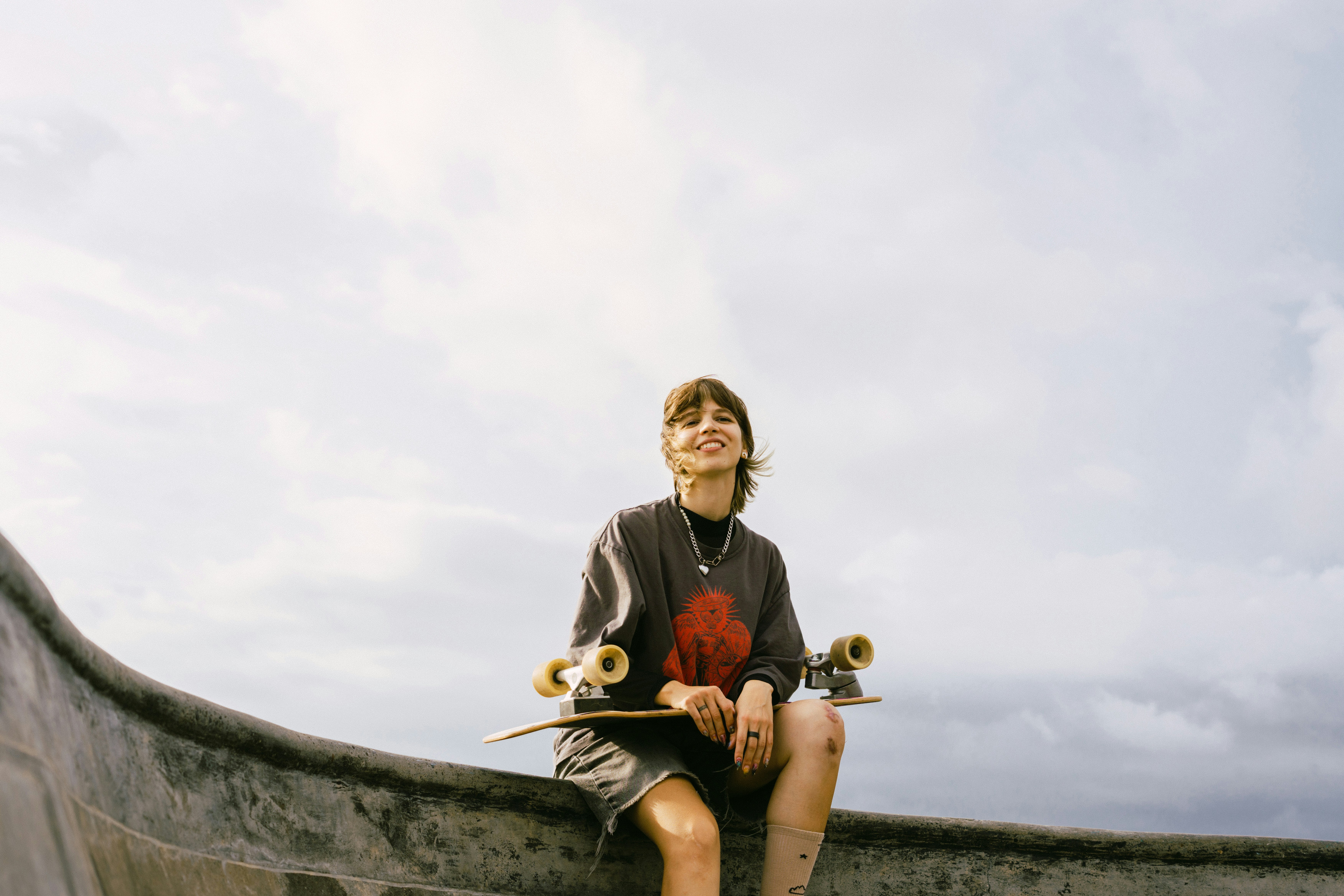 Young woman with skateboard sitting outdoors on cloudy day