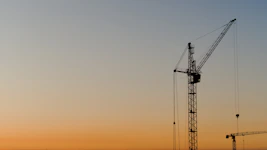 Construction cranes silhouetted against a sunset sky