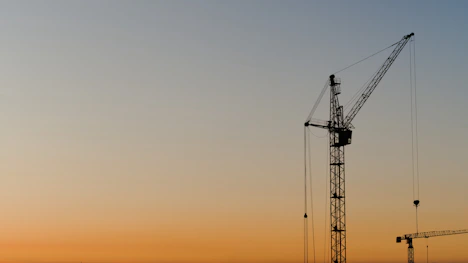 Construction cranes silhouetted against a sunset sky
