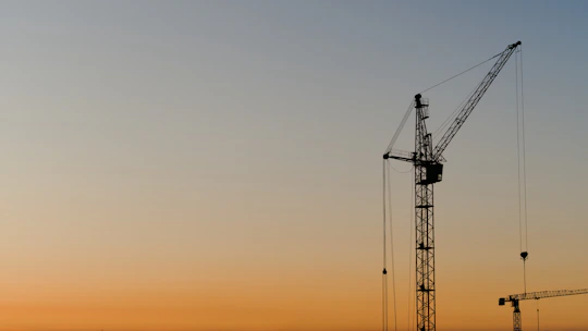 Construction cranes silhouetted against a sunset sky