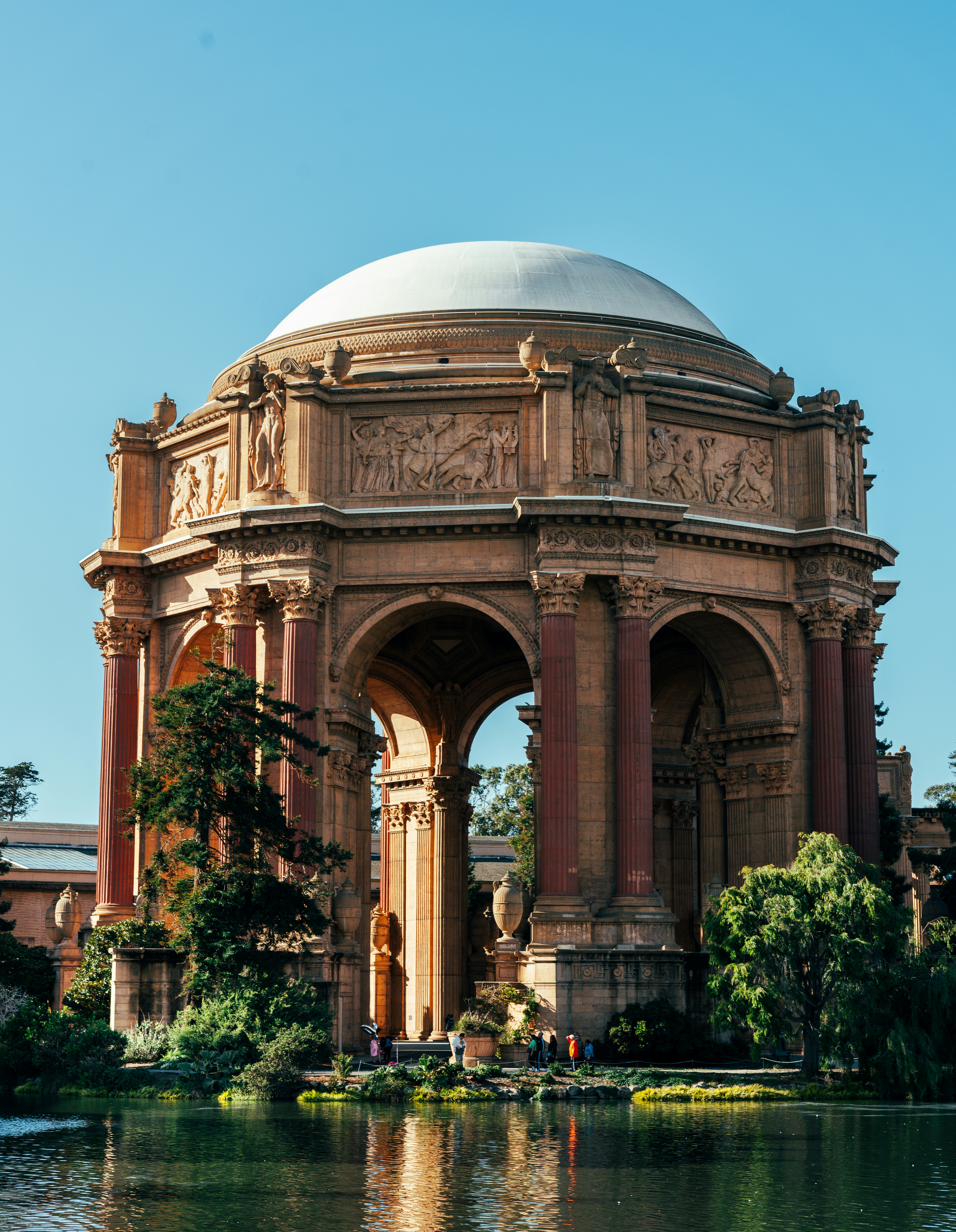 Grand domed building with arches and columns by water.