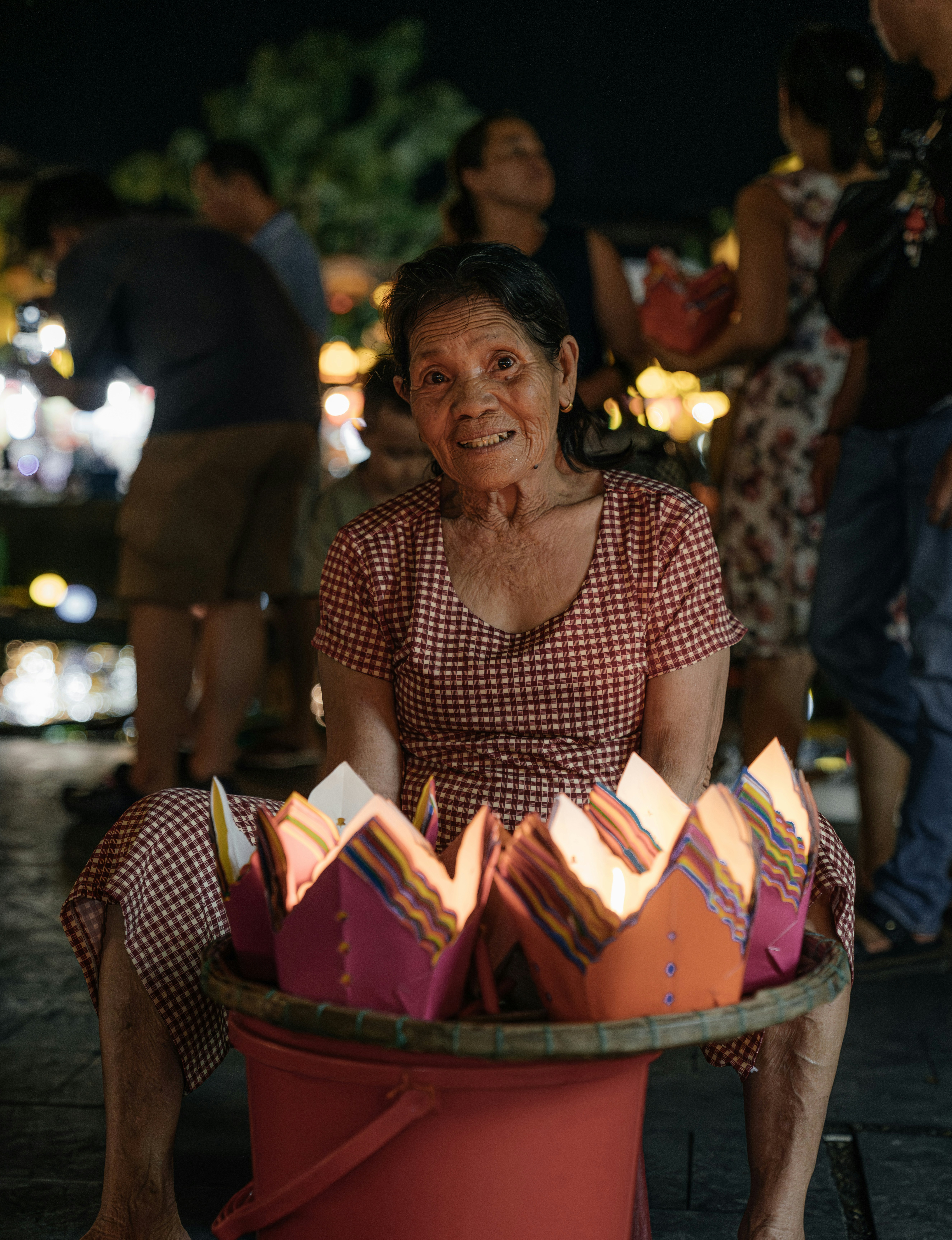 Elderly woman selling lotus lanterns at night.