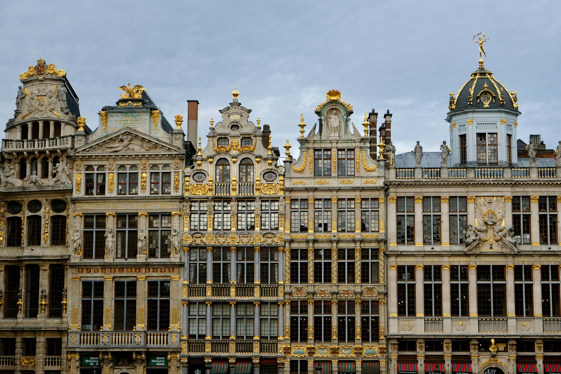 Ornate historic buildings with golden accents under cloudy sky.