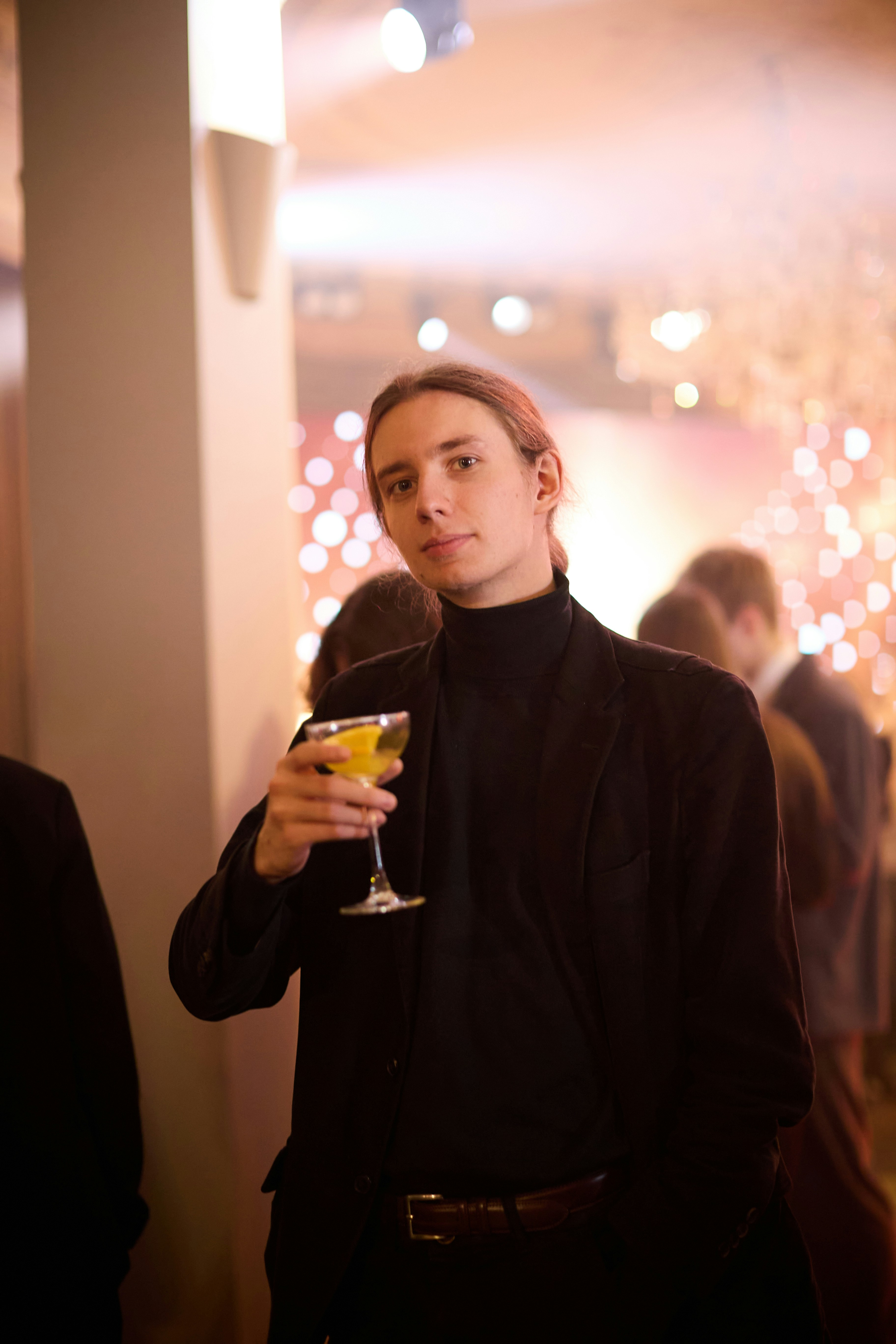 Man in black turtleneck and jacket holding cocktail
