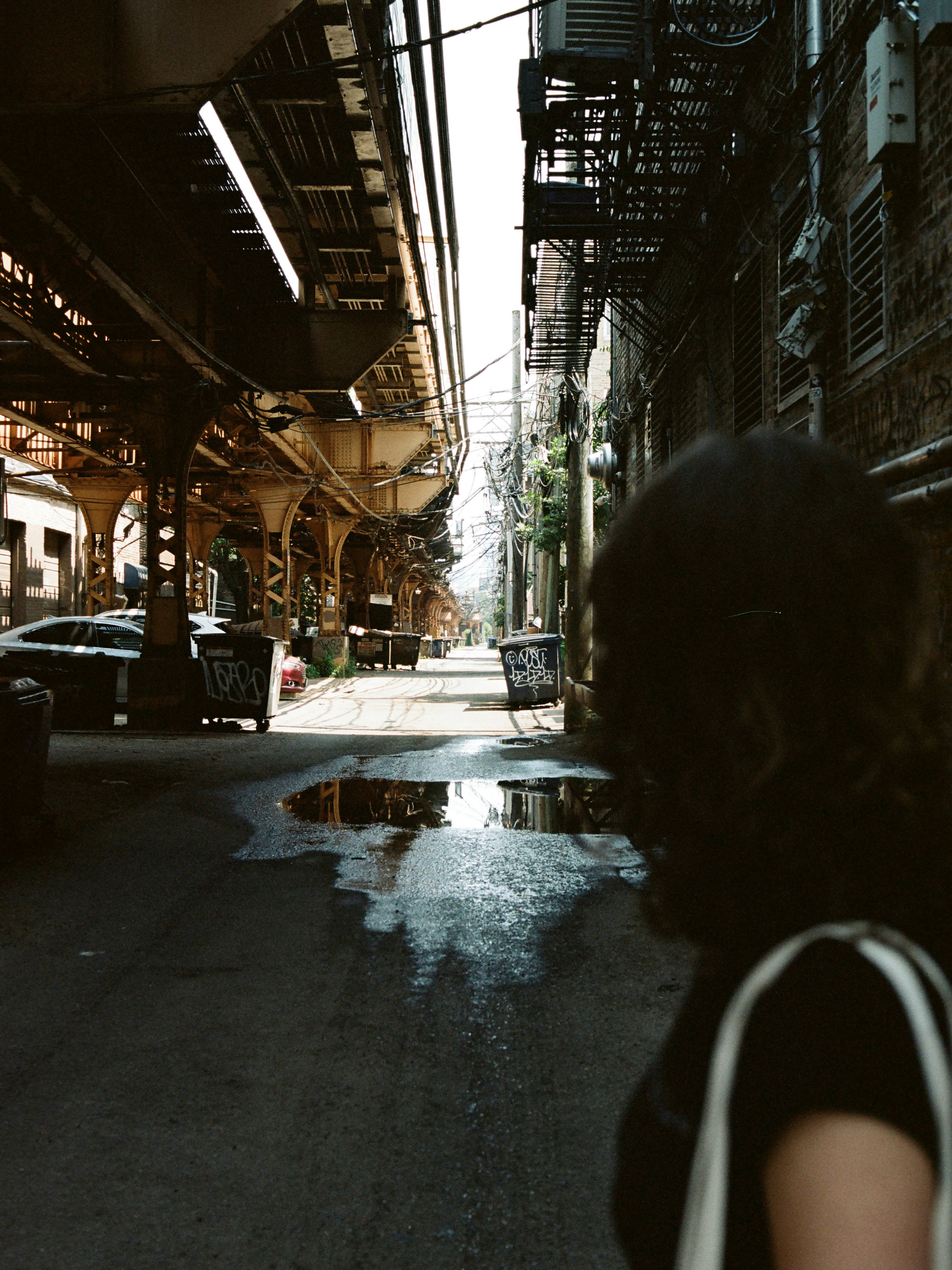Une personne marche dans une ruelle urbaine sous des voies ferrées surélevées.