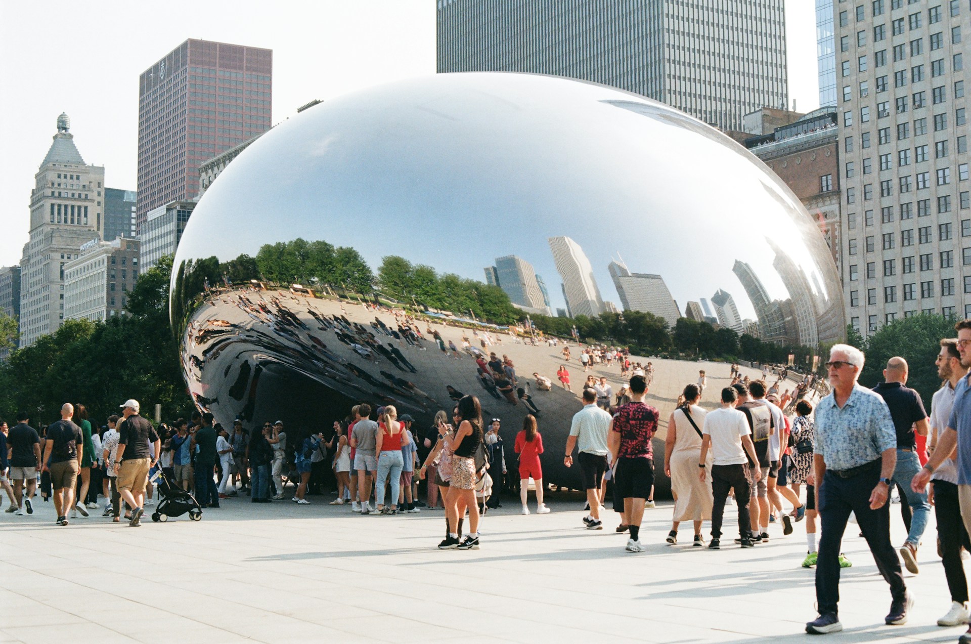 Cloud gate sculpture reflecting chicago cityscape with people walking.